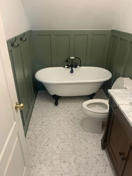 Small bathroom with freestanding tub, toilet, vanity, and green paneled walls.