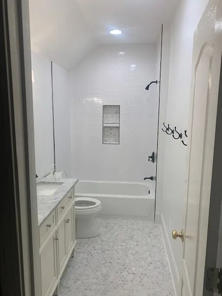 Small white bathroom with tub, toilet, sink vanity, and light gray tile floor