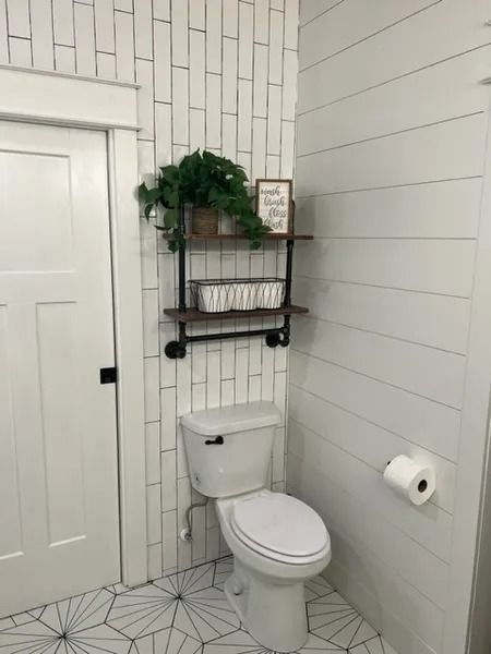 Small white bathroom with toilet, toilet paper holder, and black wall shelf with decor above it