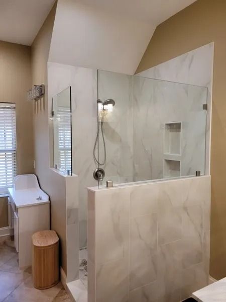 Modern beige bathroom with glass shower, white vanity, window, and wooden stool