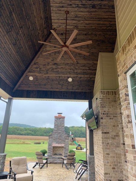 Covered patio with wooden vaulted ceiling, ceiling fan, brick grill, and chairs overlooking a grassy yard