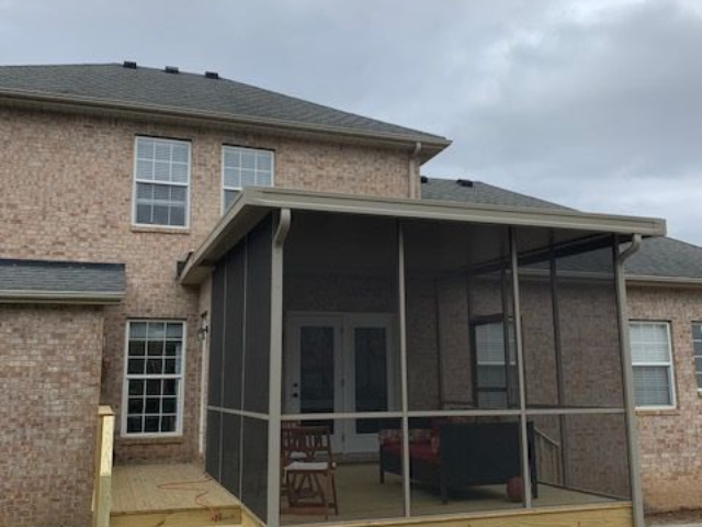Brick apartment building with a covered porch and stairs, seen from a driveway under a cloudy sky