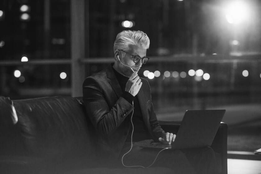 Man with glasses and oxygen tube, works on laptop at night.