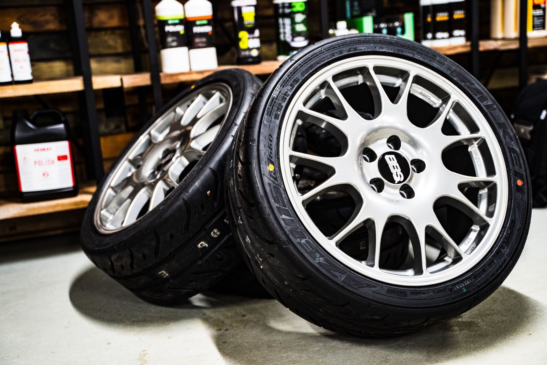 Black alloy car wheel with yellow brake caliper and red bodywork visible at the edge.