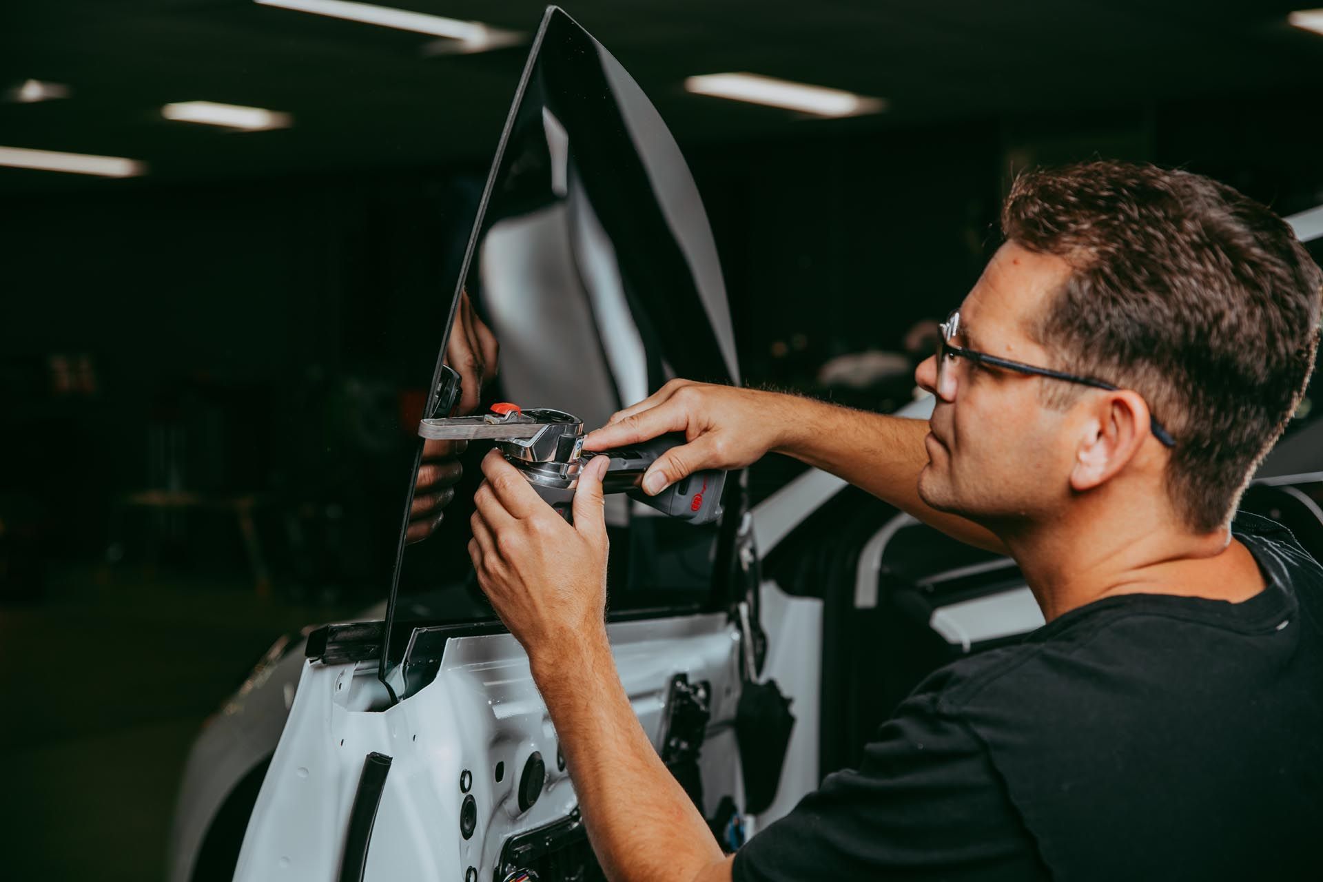 Mechanic adjusting a white car's wiring under a raised hood in a dim garage