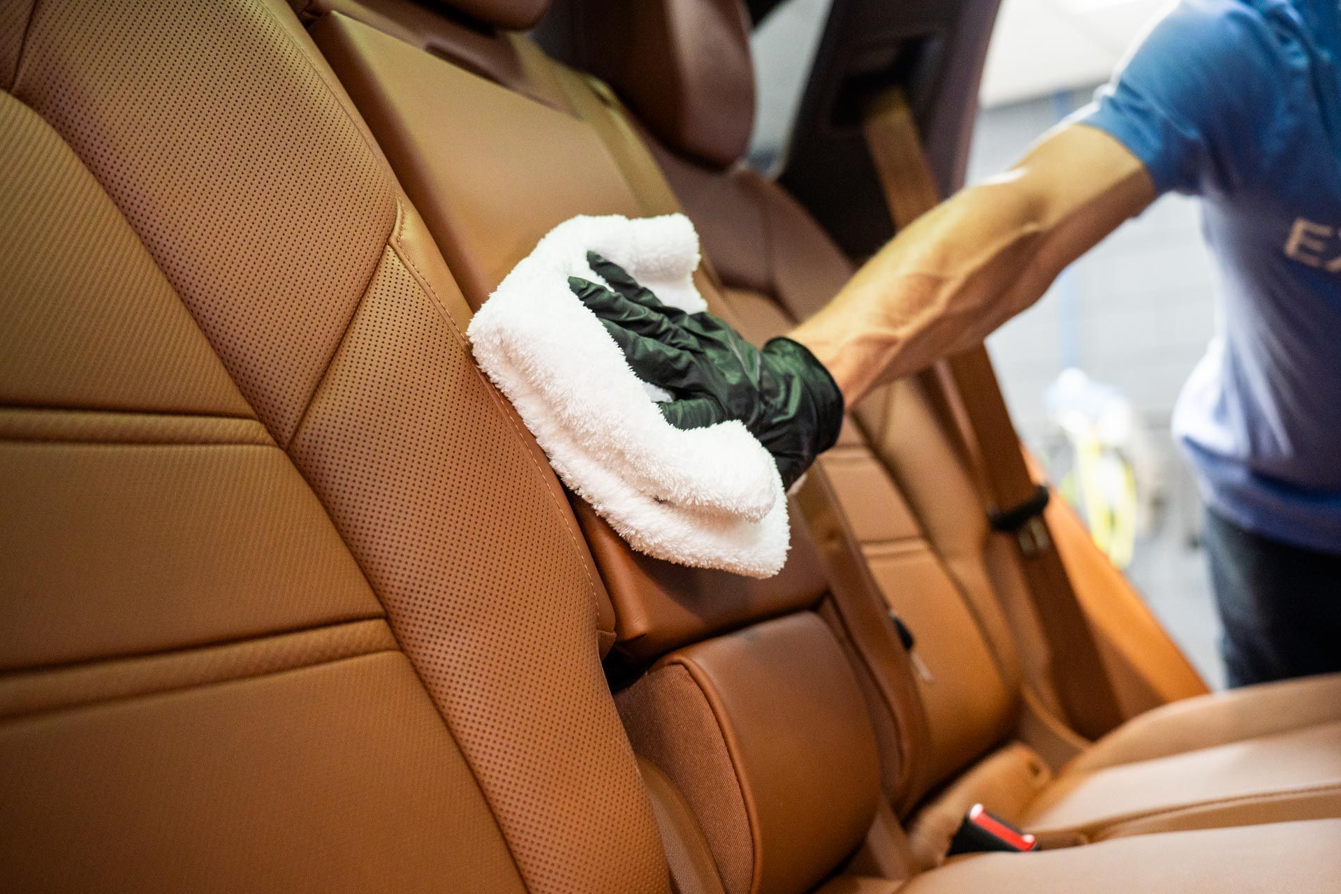 Person cleaning a tan car seat with a cloth inside a car interior.
