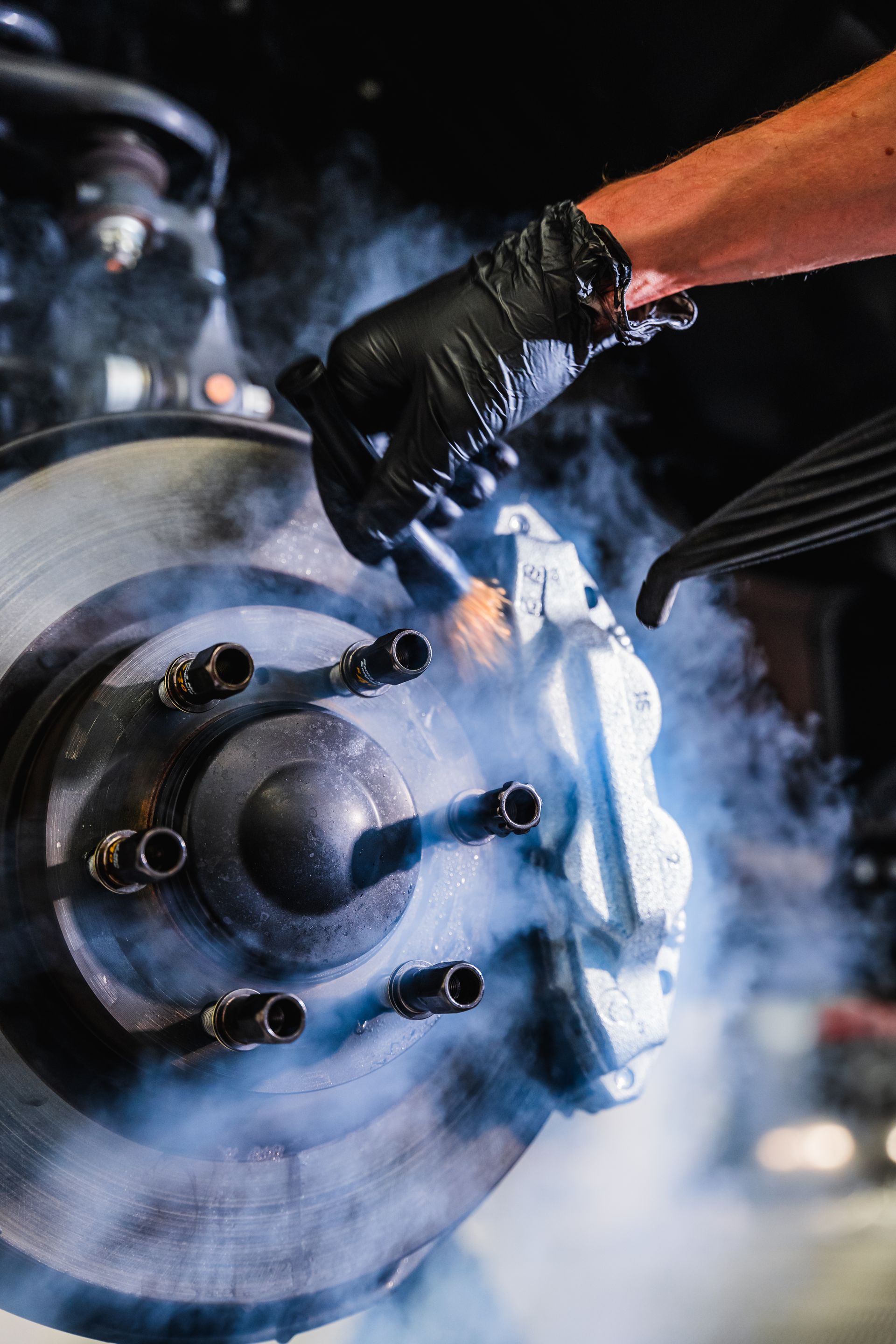 Gloved hand loosening a car wheel lug nut with smoke or steam around the brake rotor