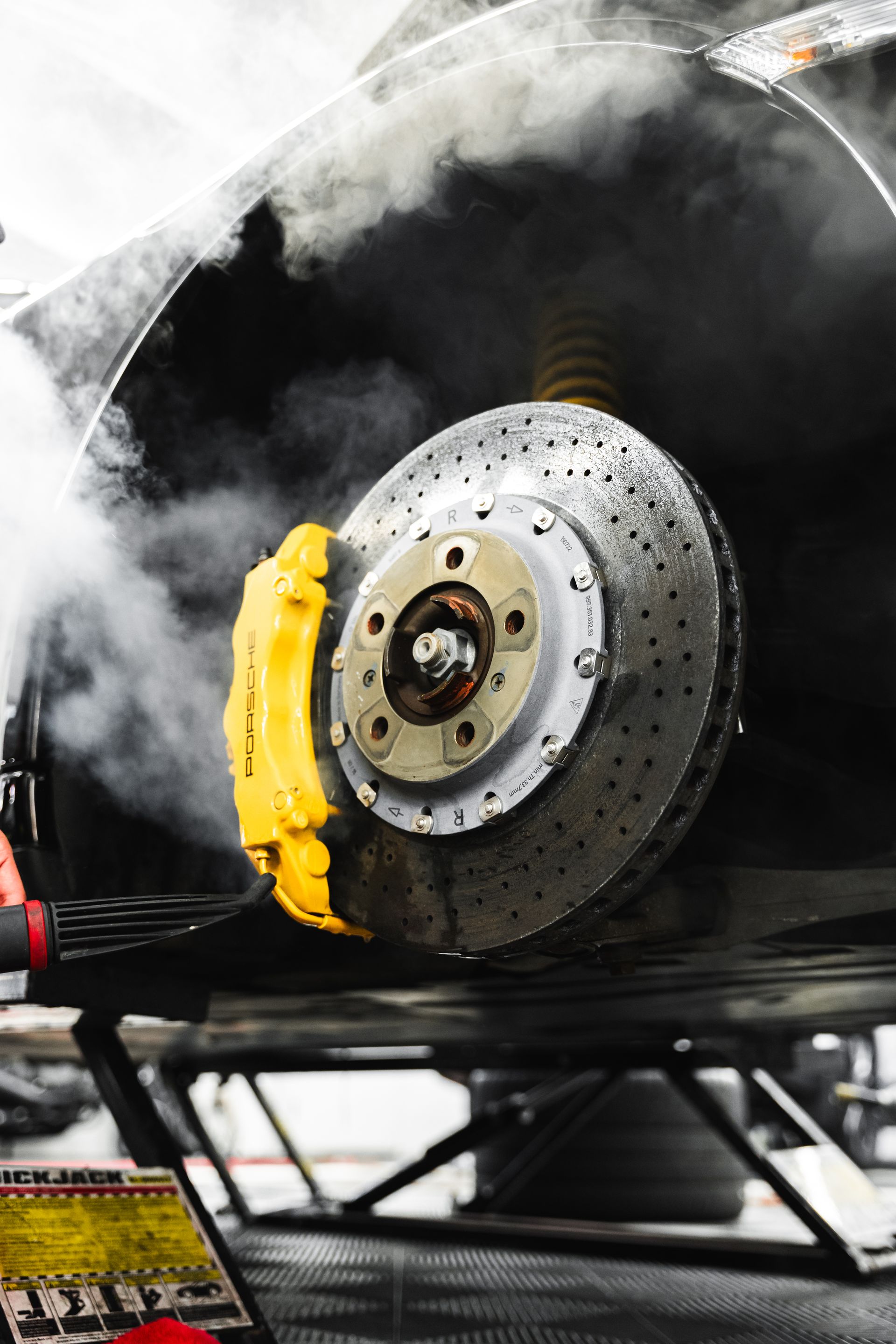 Close-up of a car brake rotor glowing hot with smoke and a yellow caliper underneath the wheel arch