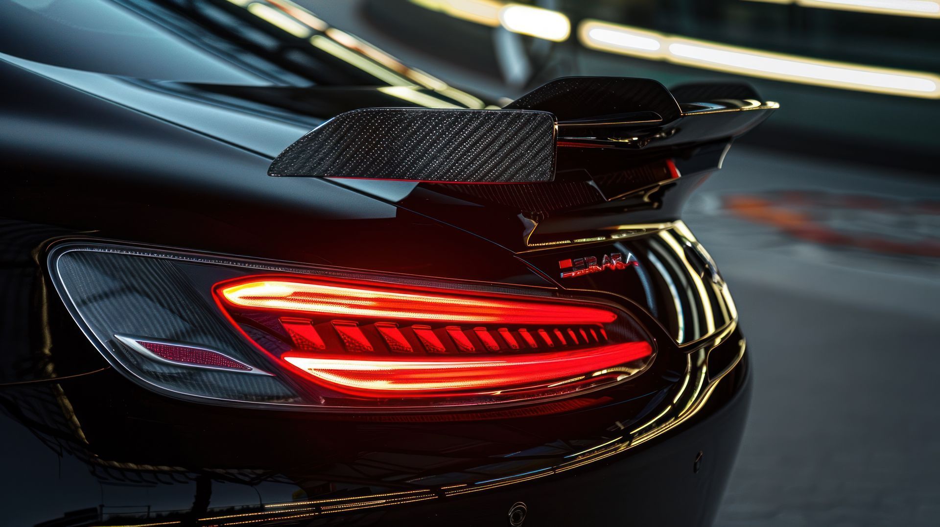 Close-up of a black sports car’s rear with glowing red taillight and carbon-fiber spoiler