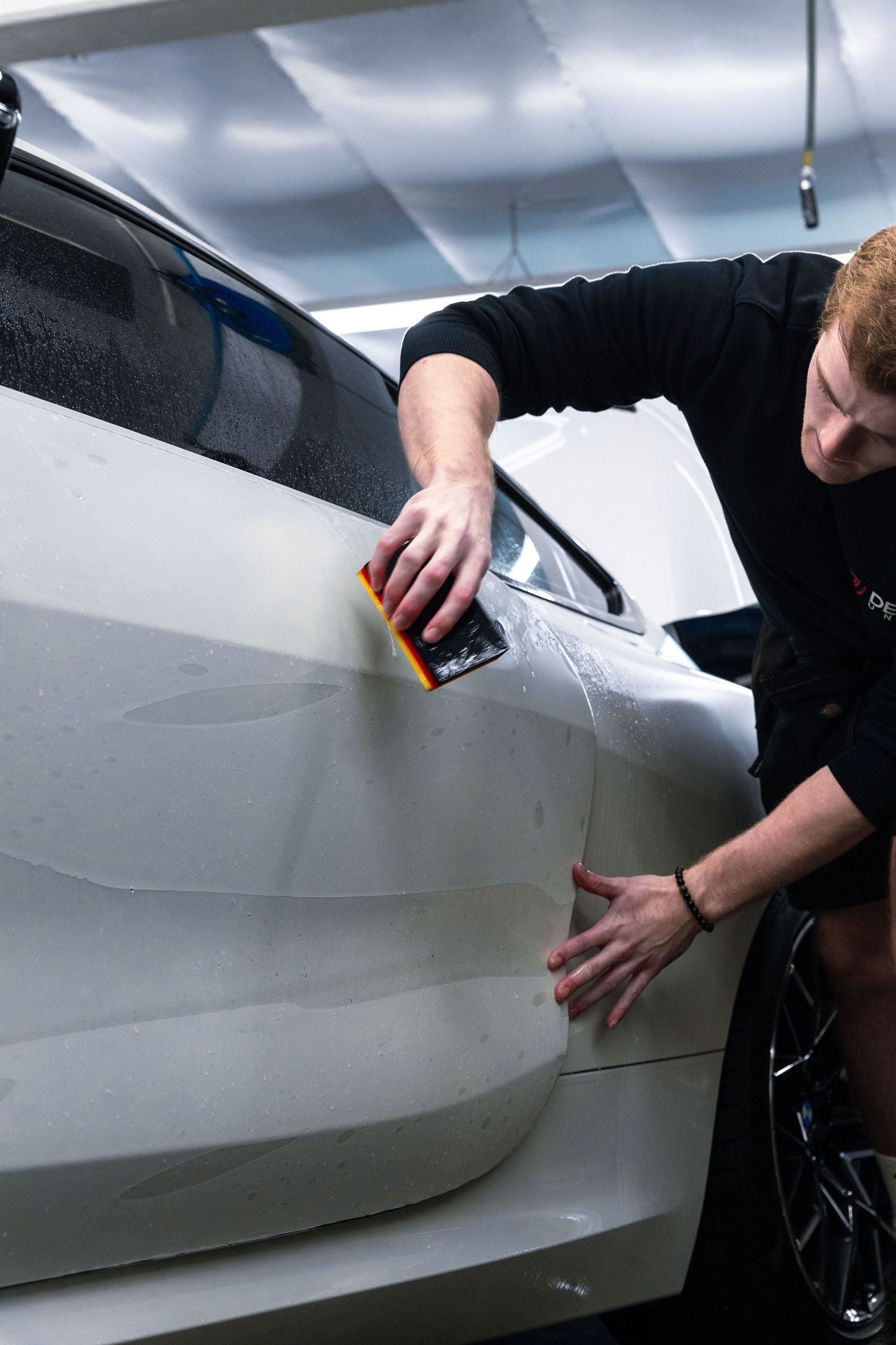 Person wipes a silver car door with a cloth in a garage or workshop.