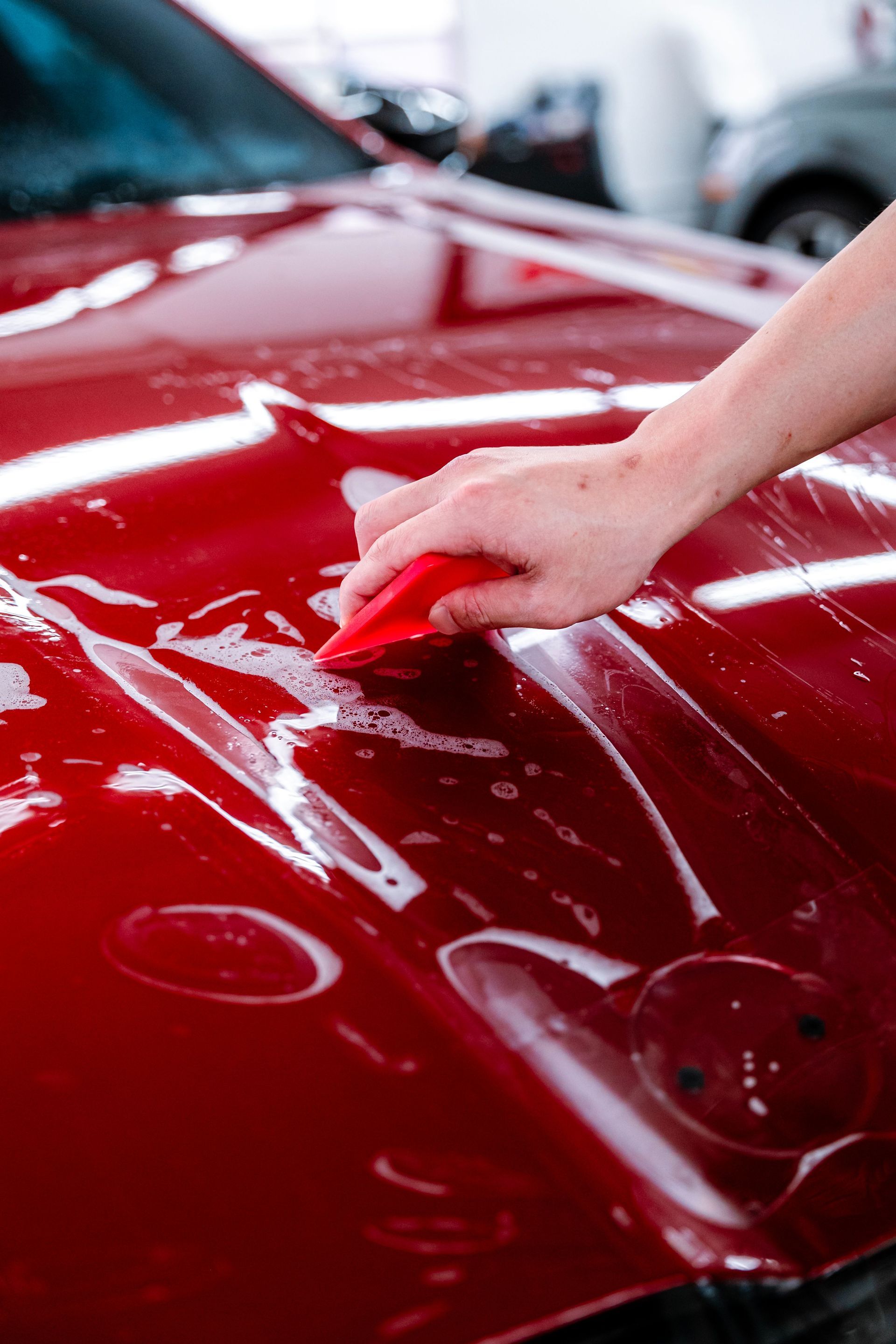 Hand polishing a glossy red car hood in a garage