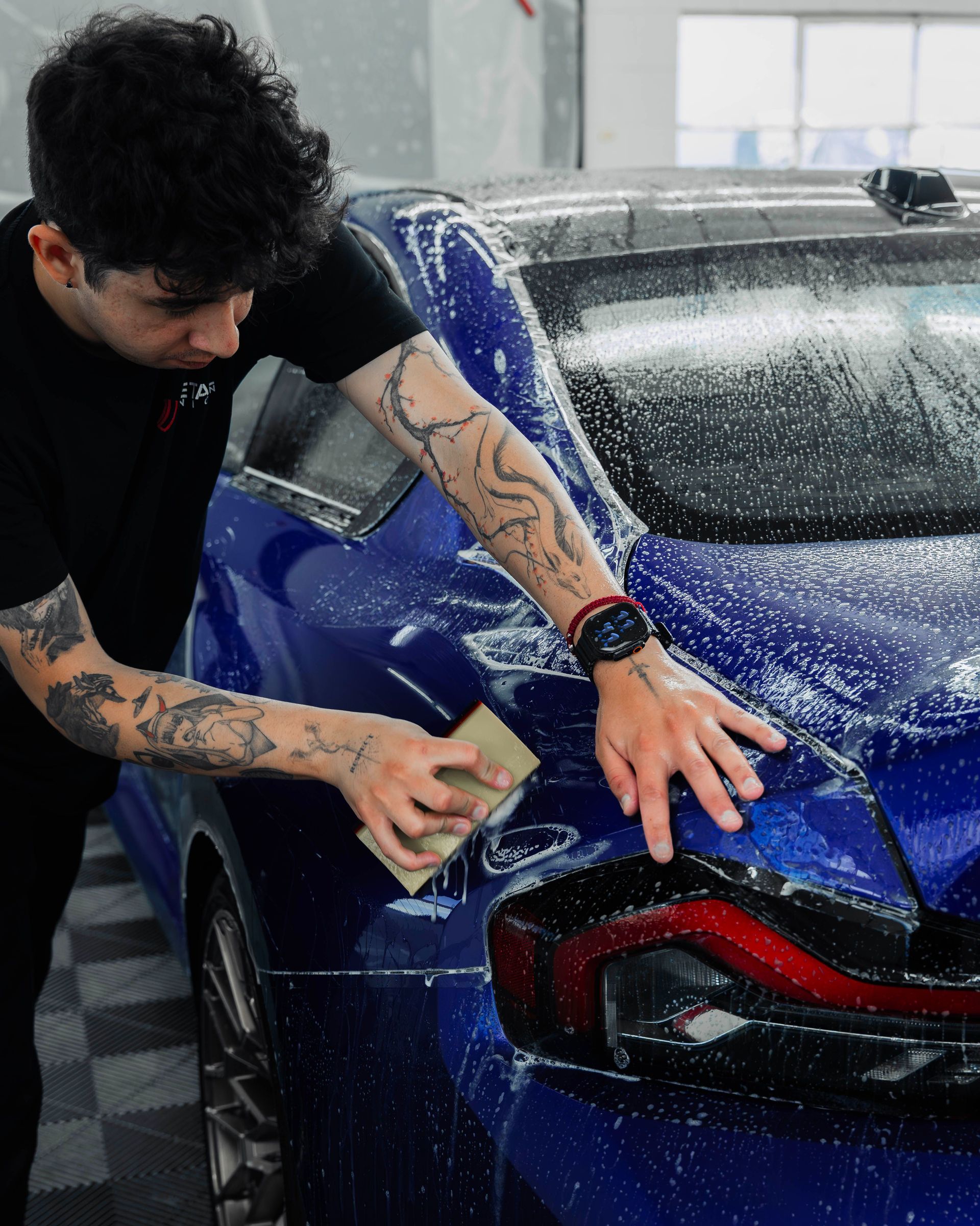 Person washing a blue sports car with soap in a car wash.