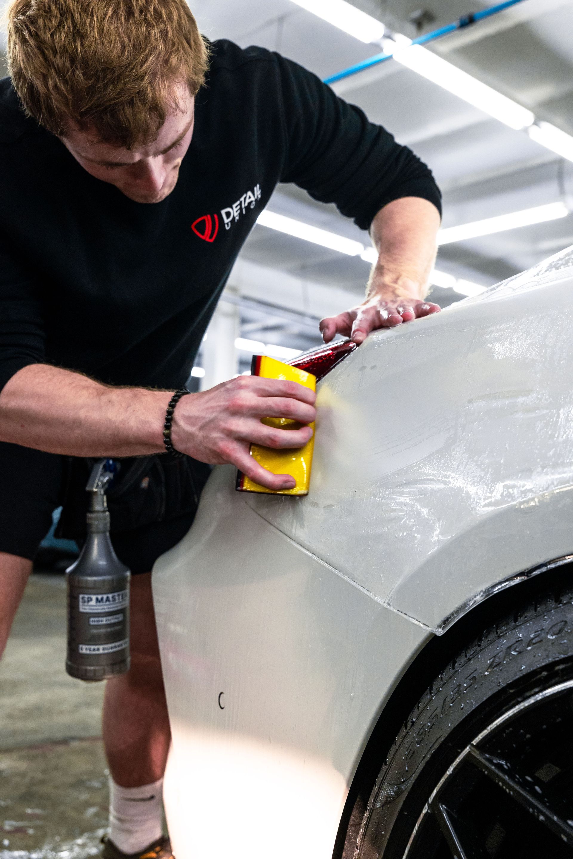 Man polishing a silver car panel with a yellow cloth in a garage