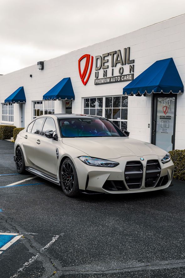 Gray sports sedan parked outdoors in front of a white wall under a blue sky