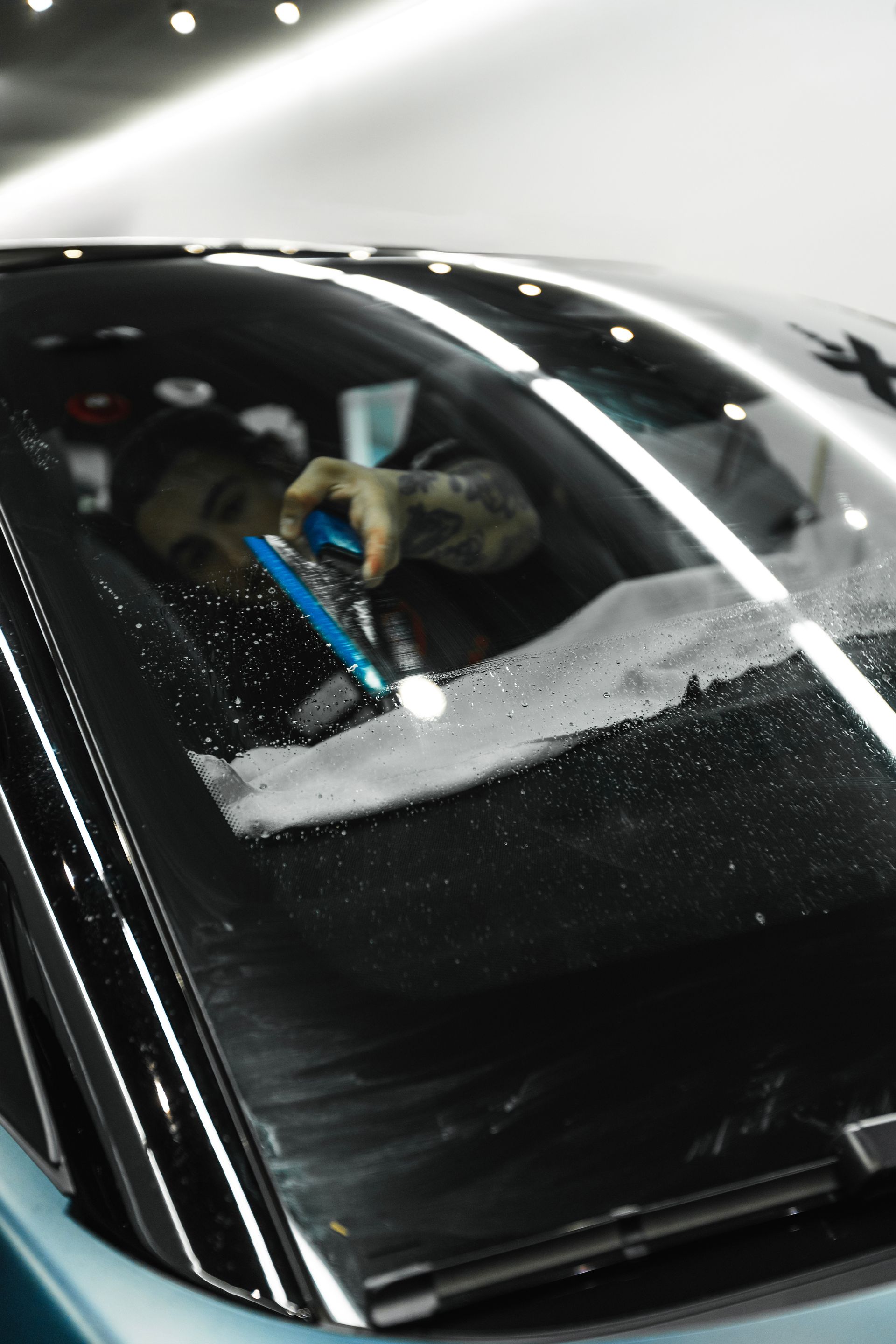 Person scraping ice off a car windshield with a blue scraper