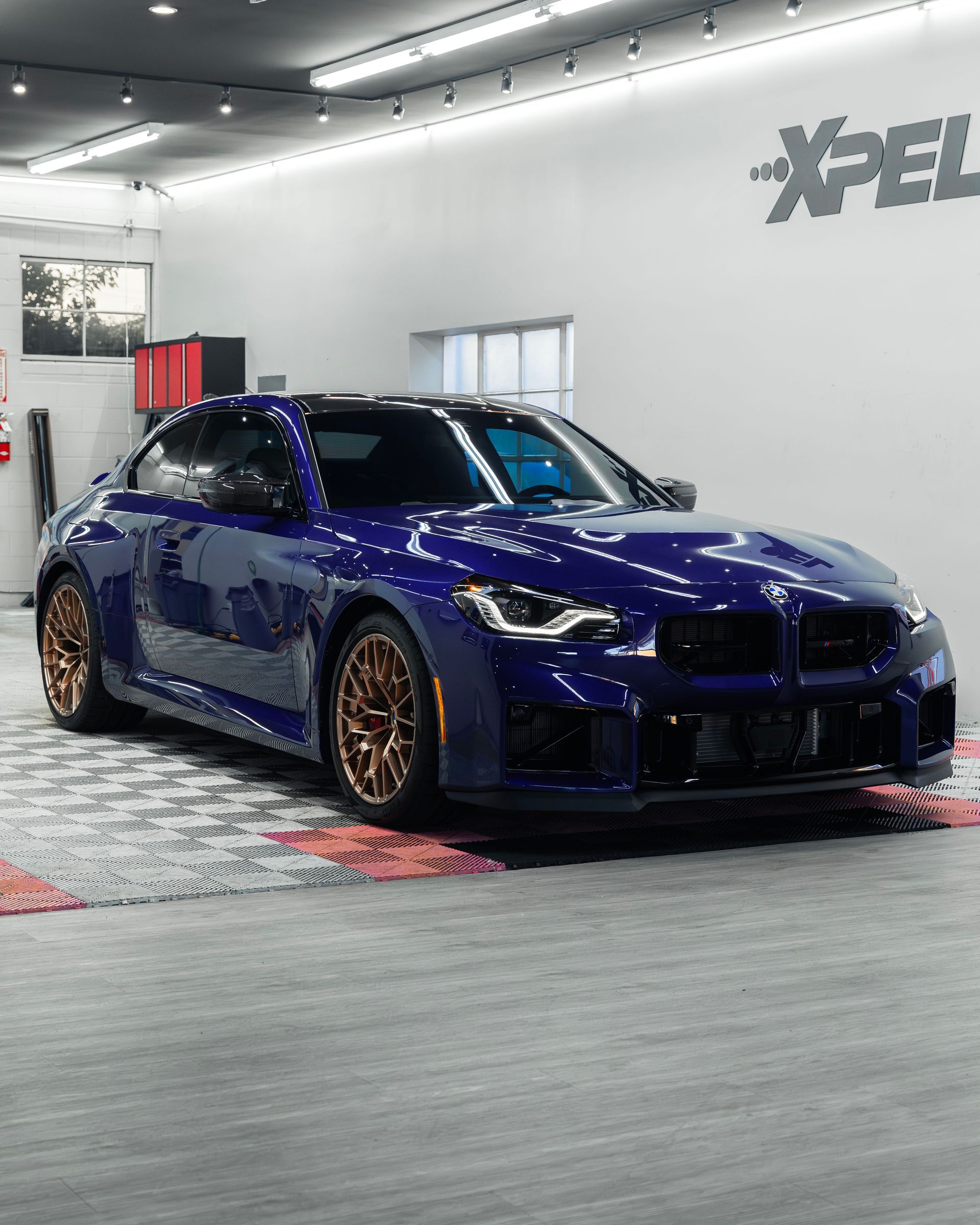 Blue sports sedan with bronze wheels displayed indoors in a car showroom