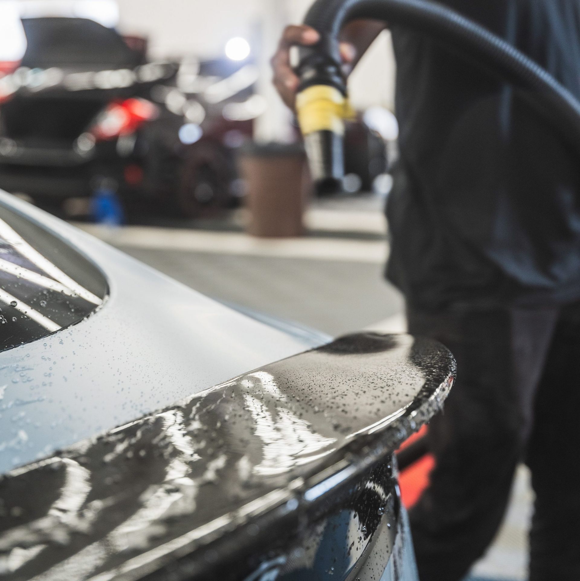 Person washing a white car’s rear spoiler with a pressure washer in a garage