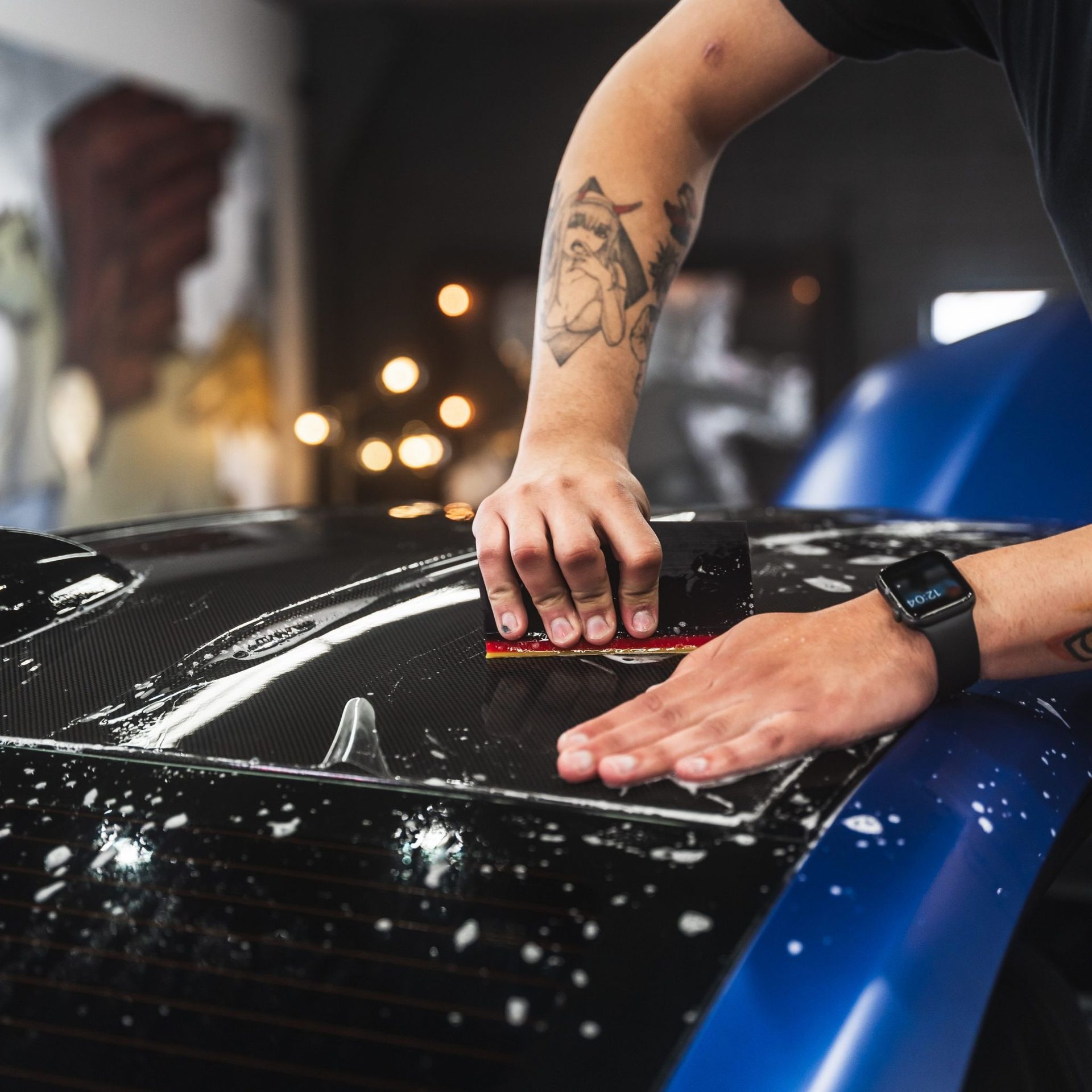 Hands polishing a glossy black car hood with a blue edge in a garage