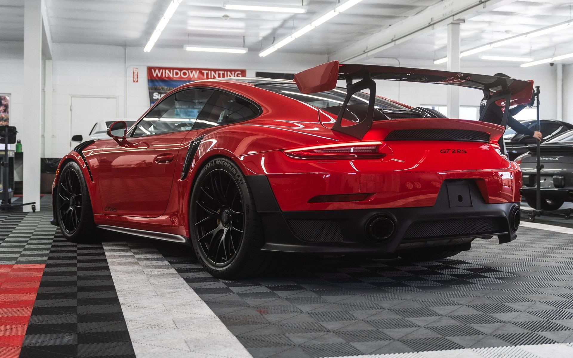 Red sports car with a large rear wing in a bright garage, shown from the rear three-quarter angle