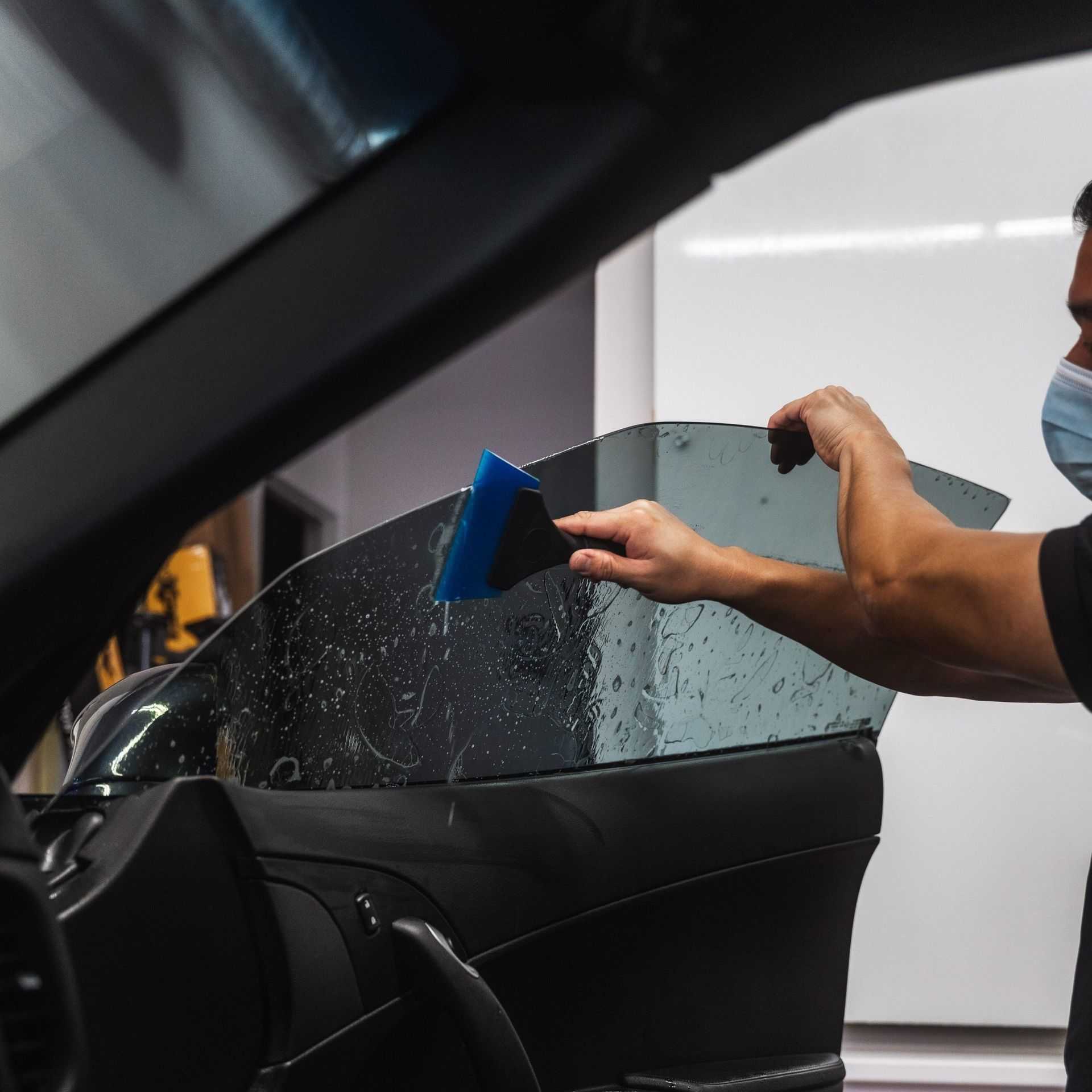 Person cleaning a car window with a blue squeegee in a detailing shop
