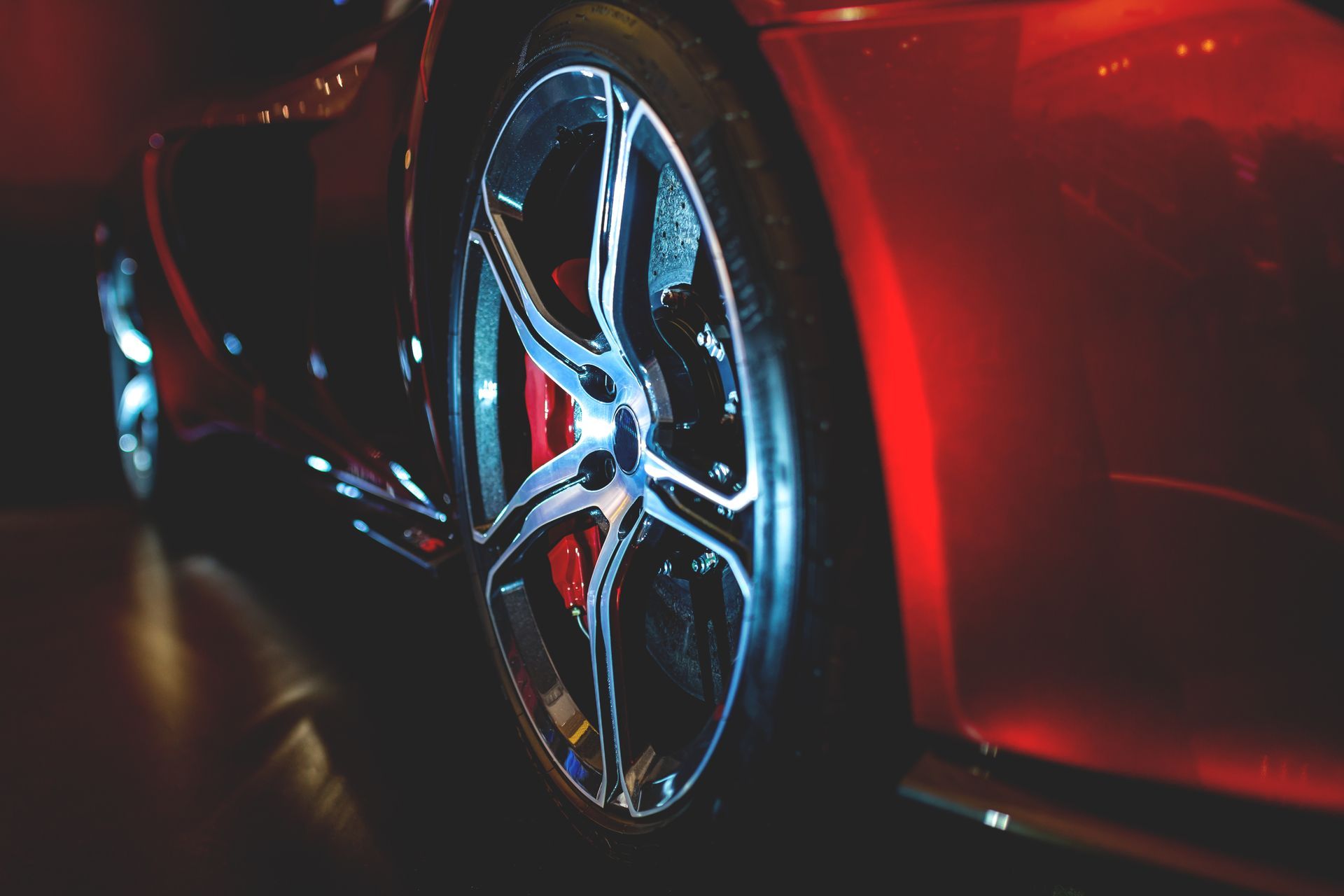 Close-up of a black sports car’s rear with glowing red taillight and carbon-fiber spoiler