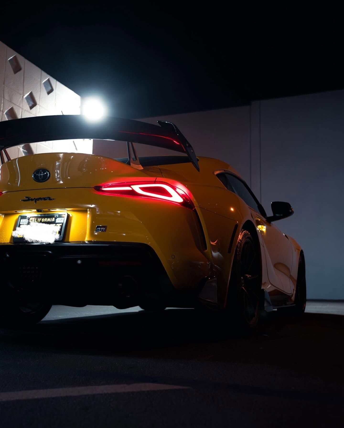 Rear side of a red sports car with black and yellow accents parked against a plain wall.