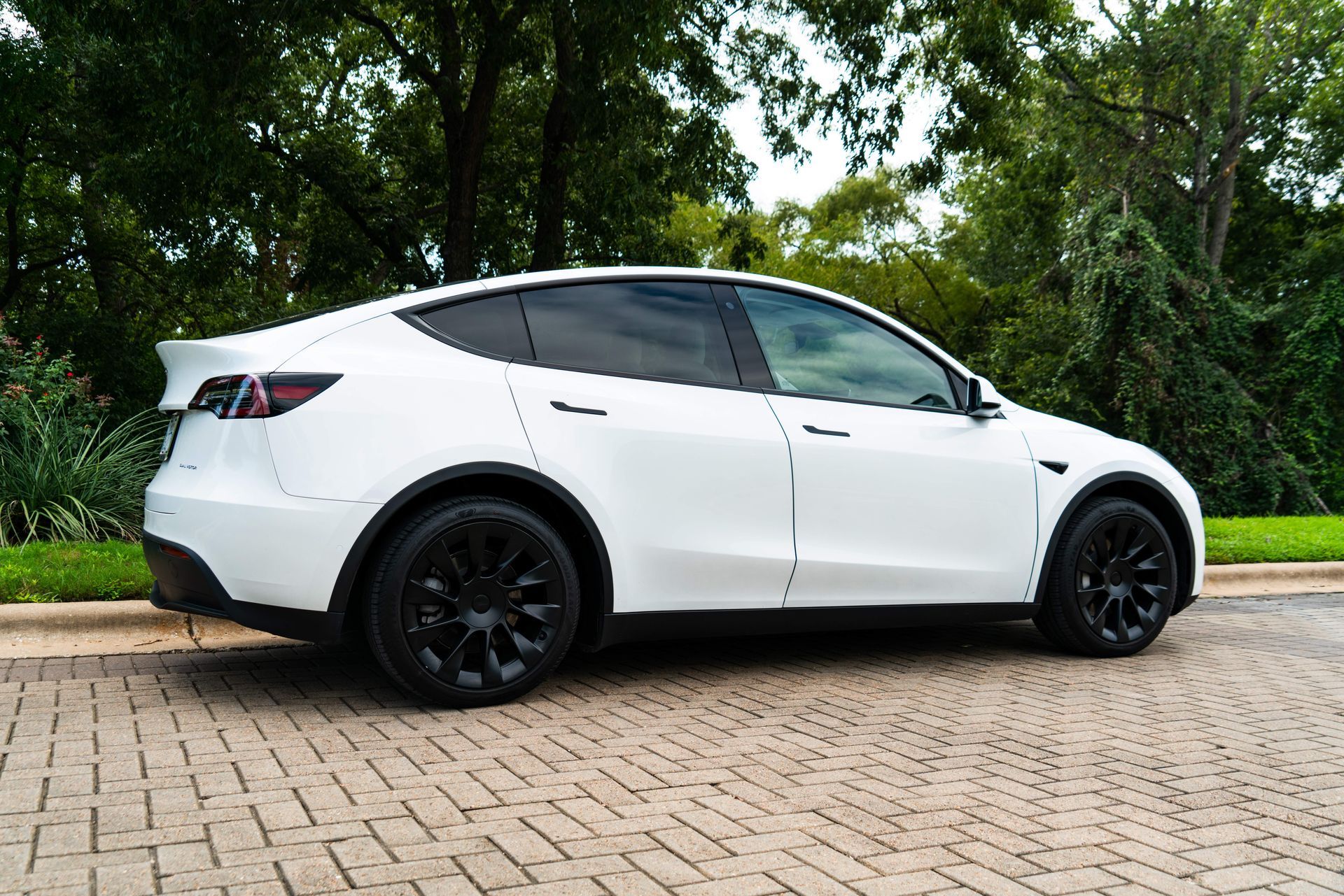 White hatchback car with black wheels parked on a brick road beside green trees