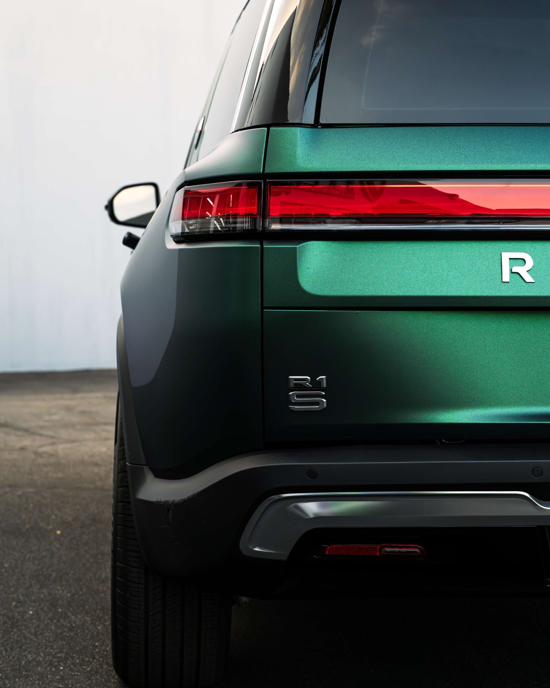 Rear view of a green SUV with a red tail light on a paved road