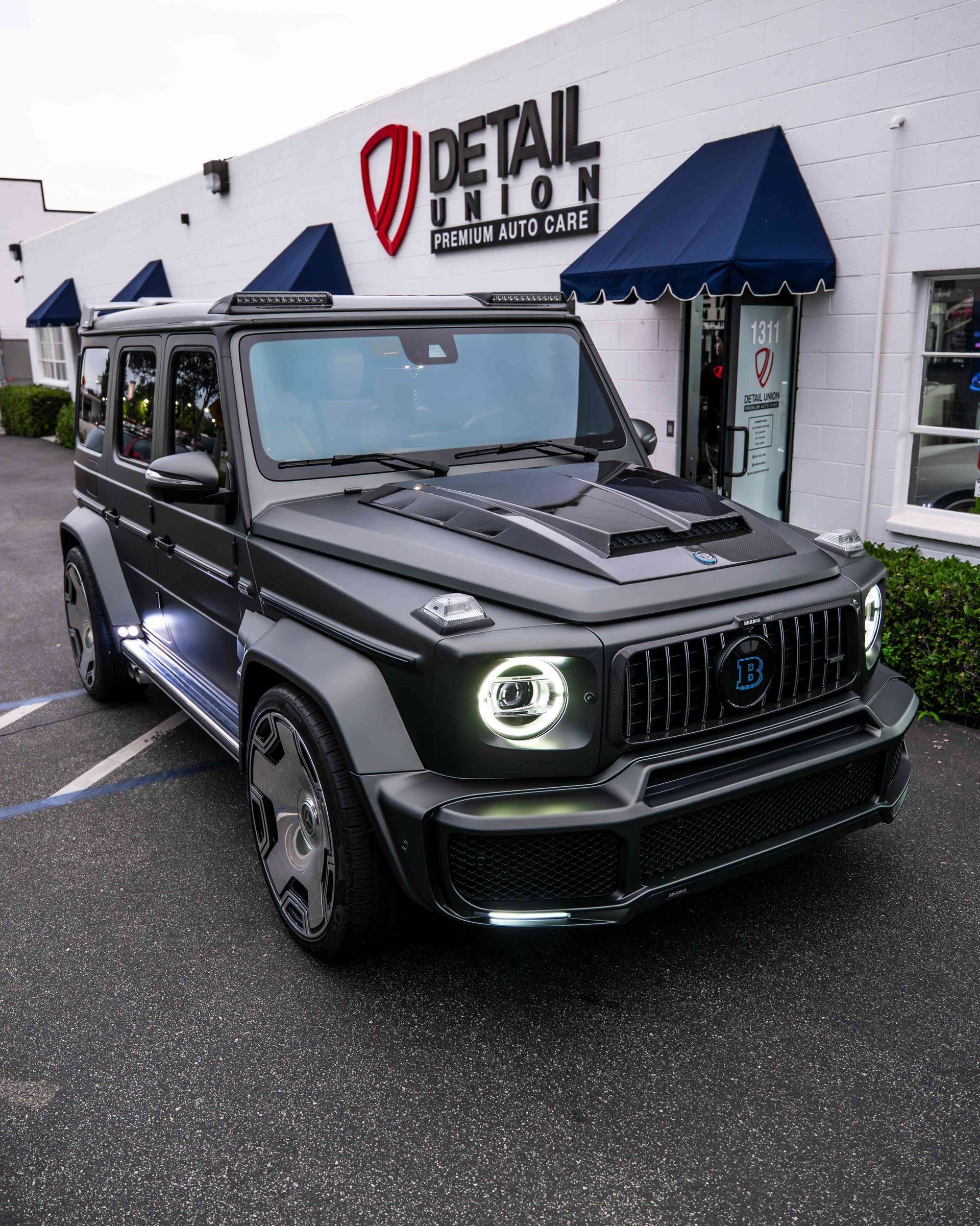 Black modified Jeep SUV parked outside a Detail King shop on a wet day