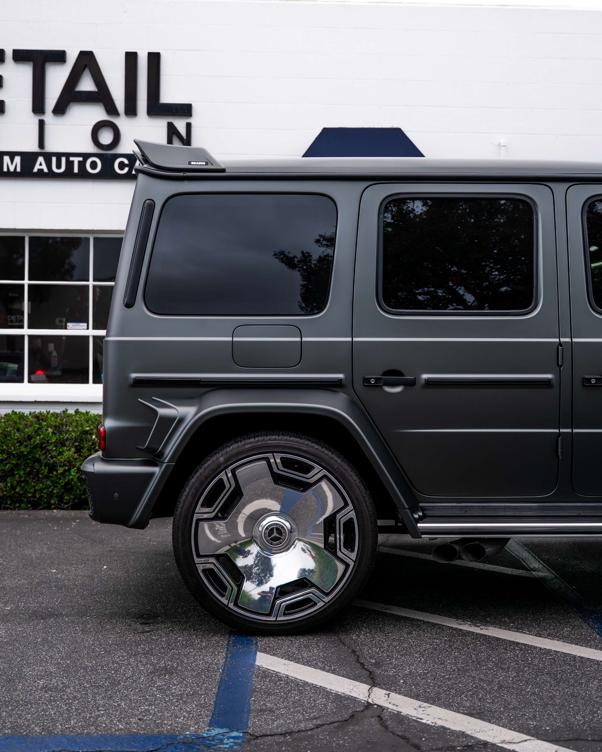 Dark gray SUV parked outside a building, showing a chrome rear wheel and side windows.