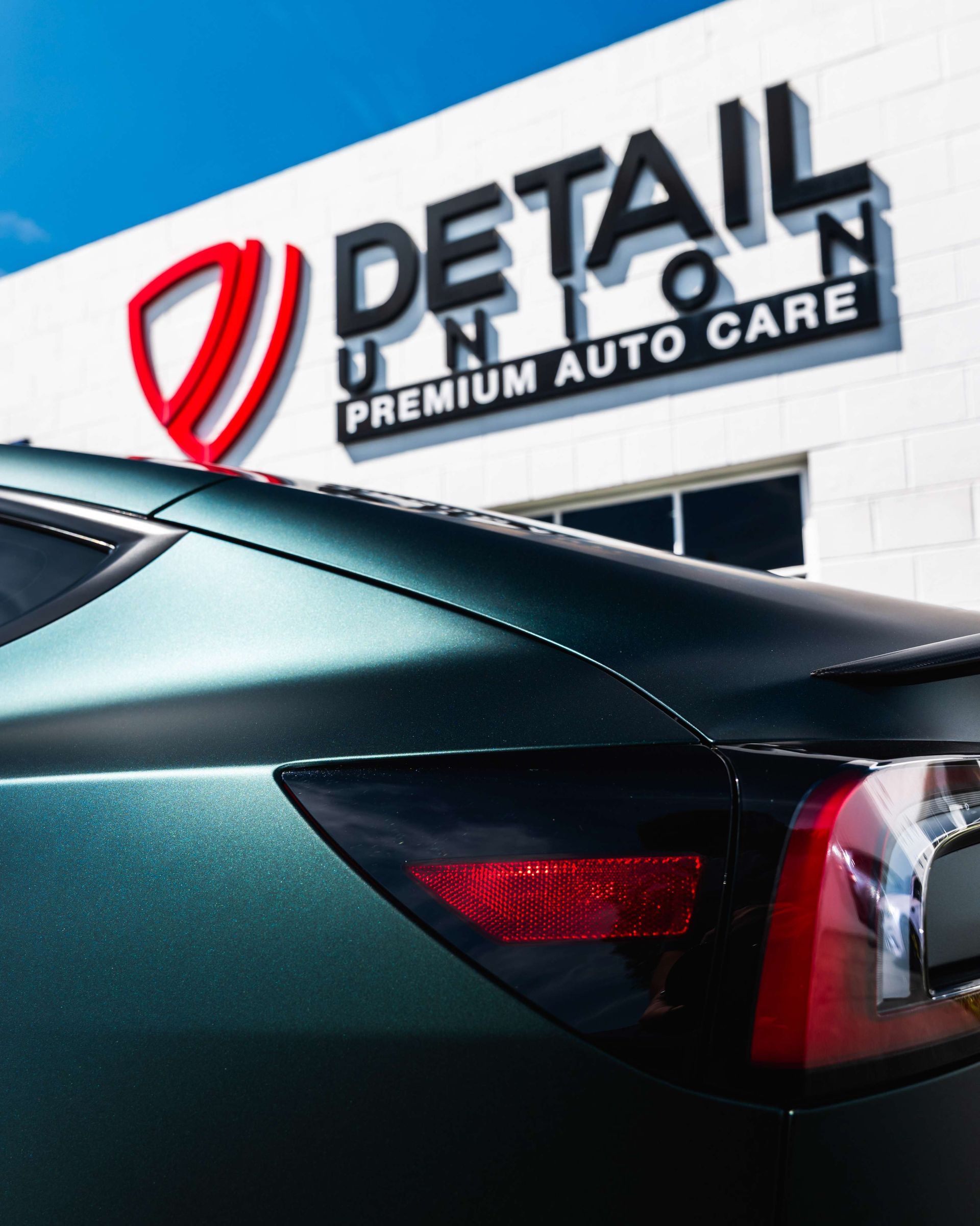 Black car parked outside Detail Premium Auto Care shop sign