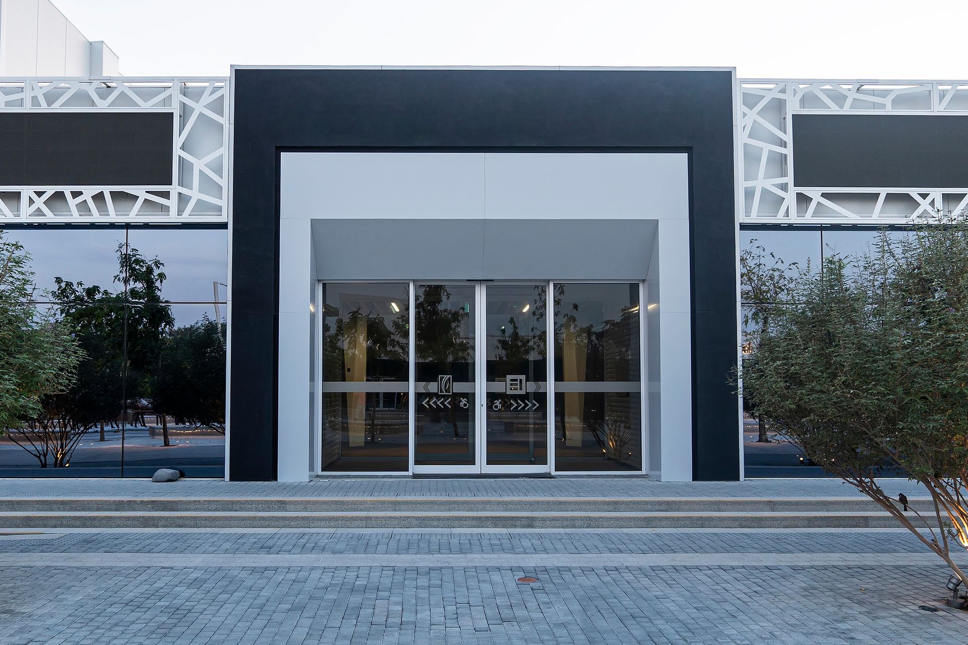 Modern building entrance with glass doors, dark frame, and steps, viewed from the front