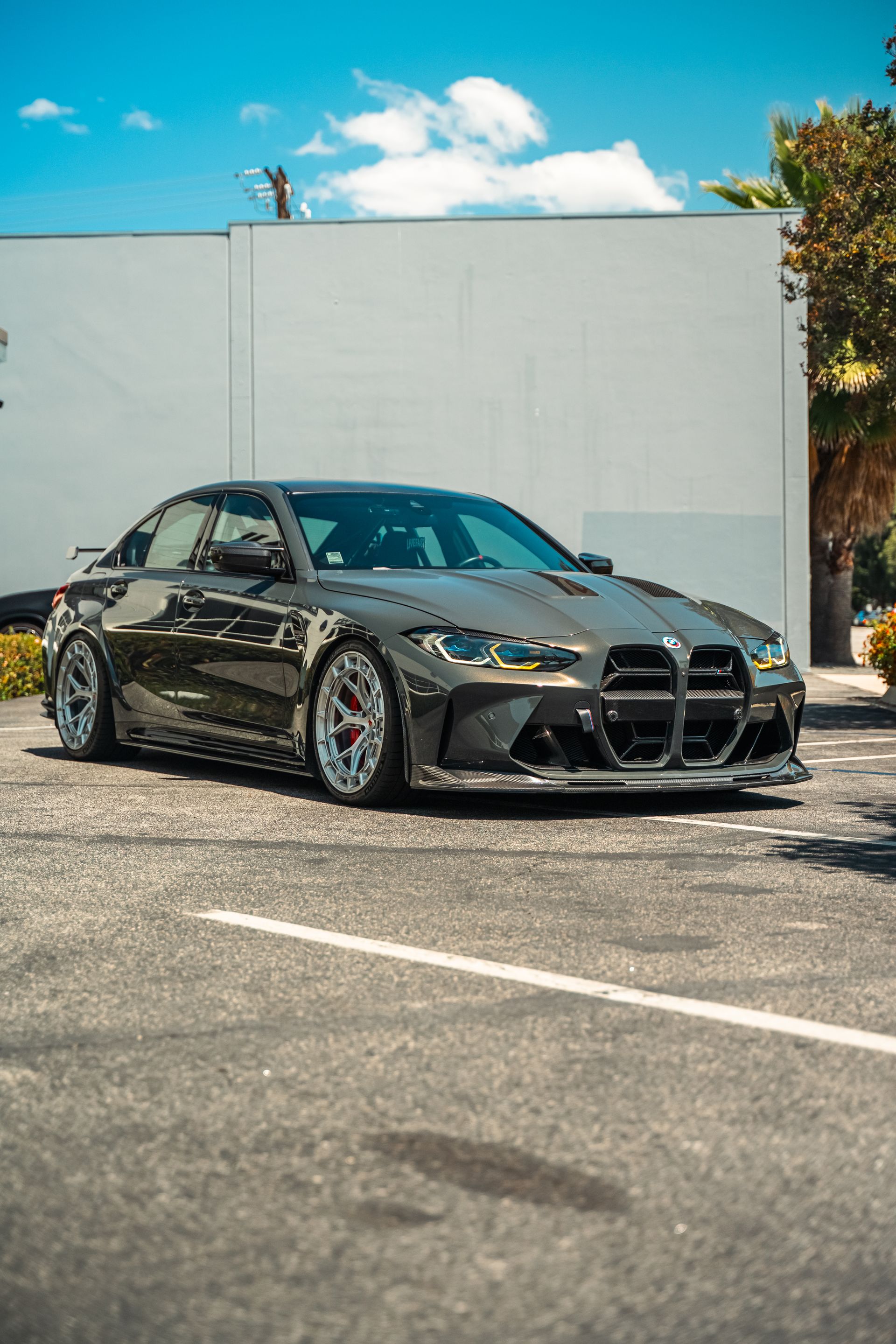 Gray sports sedan parked outdoors in front of a white wall under a blue sky