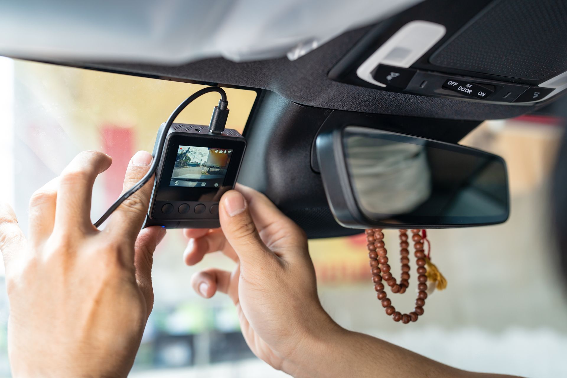 Hands mounting a dashcam on a car windshield near the rearview mirror