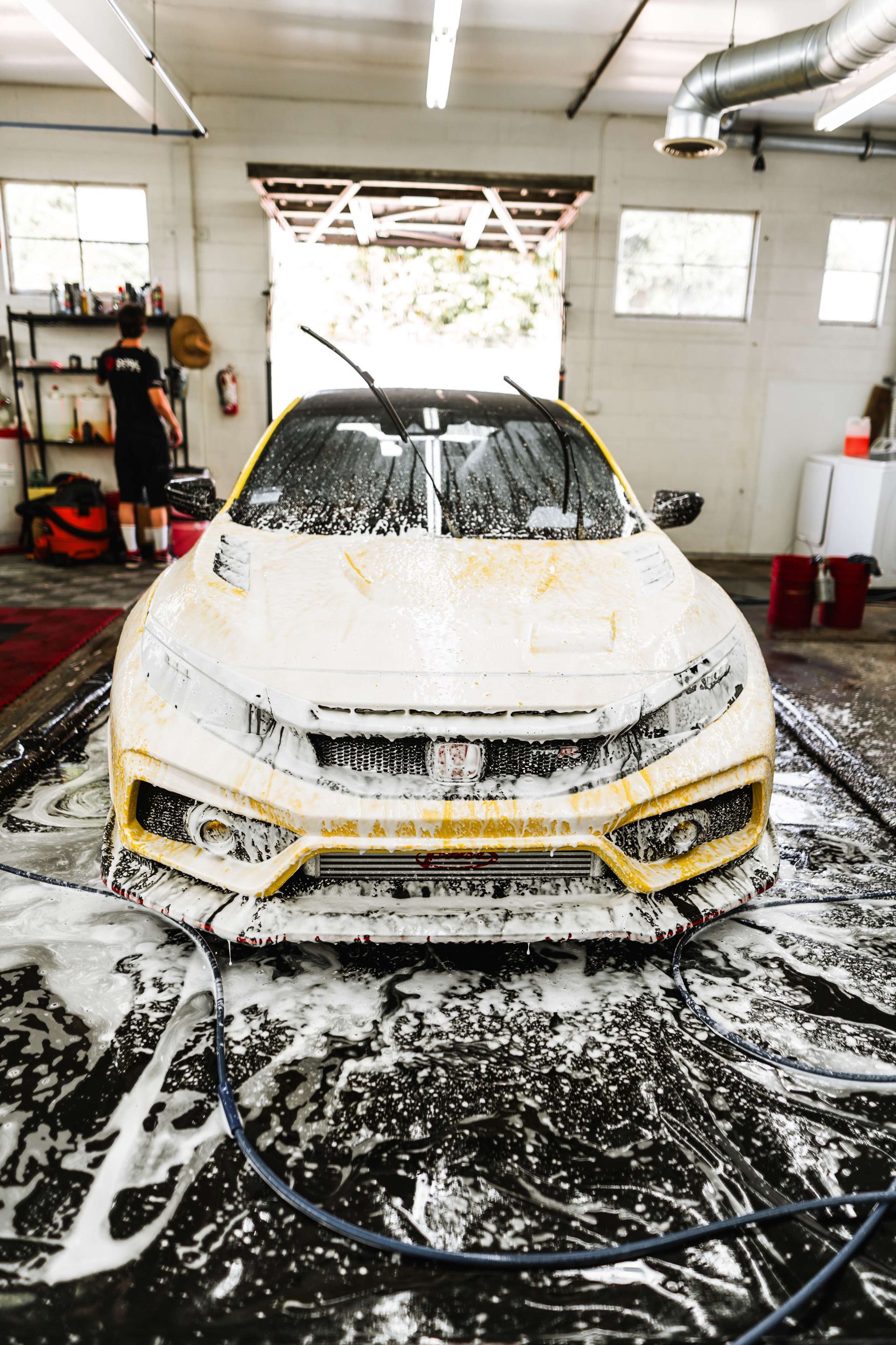 Yellow car covered in soap foam being washed in a garage car wash bay