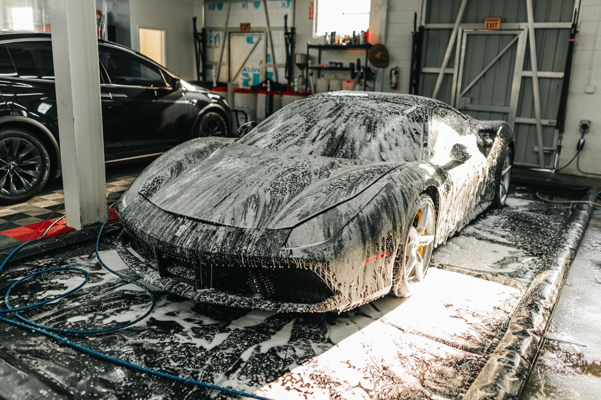 Sports car covered in soap foam being washed in an indoor car wash bay