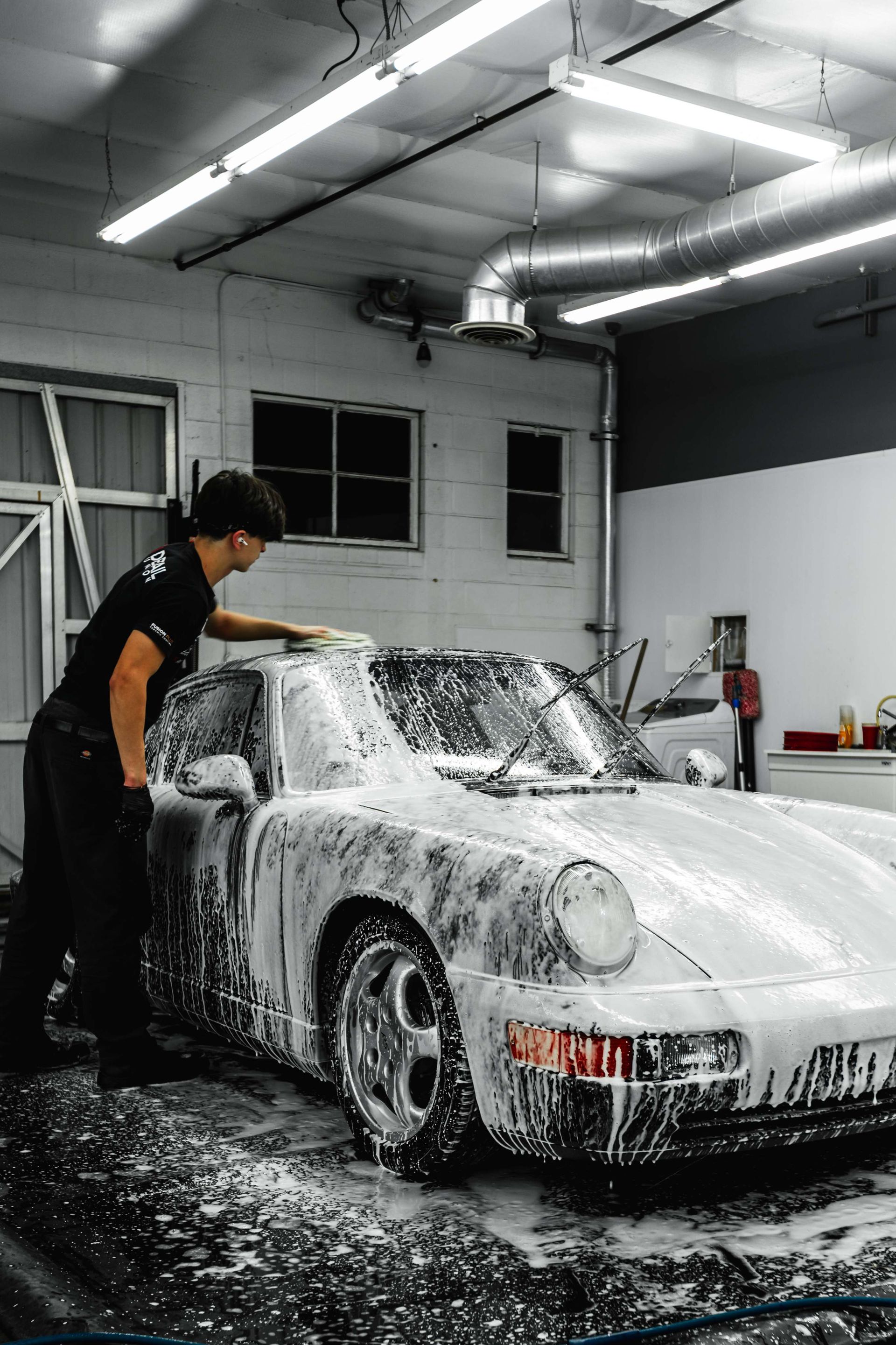 Person applying clear protective film to a blue car bumper in a workshop