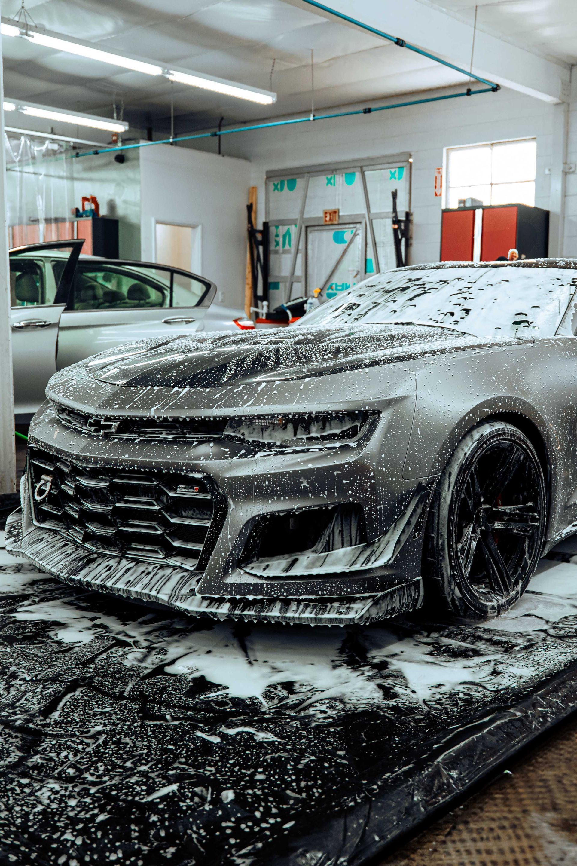 Black sports car covered in foam in a car wash bay
