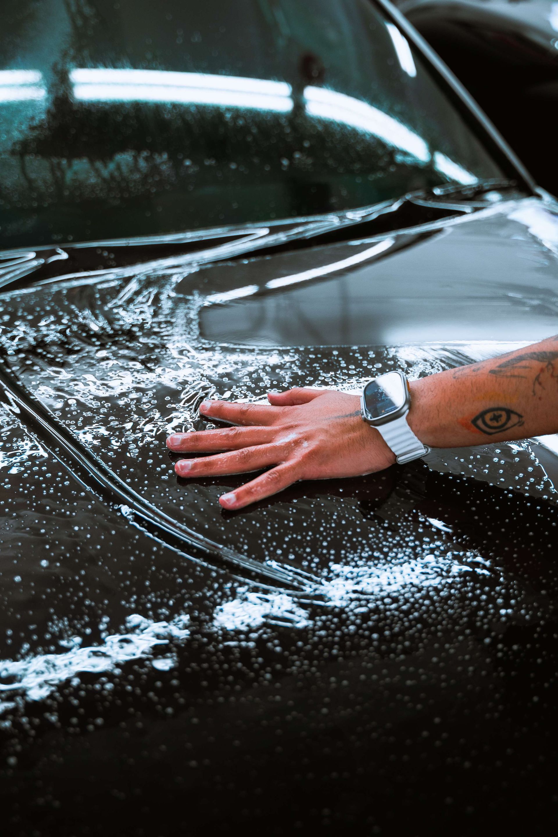 Hand scrubbing a black car hood covered in soap suds.