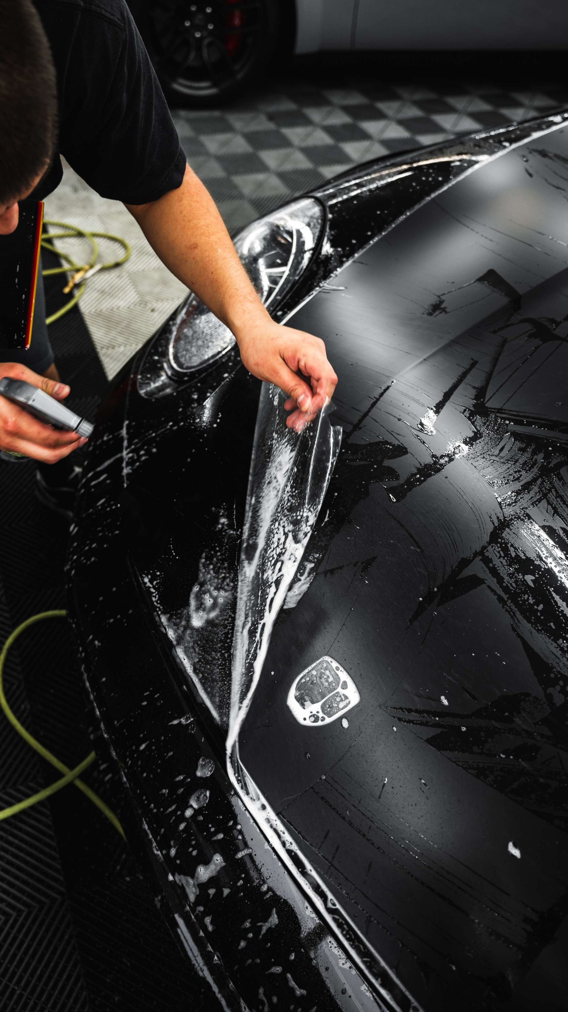 Hands applying liquid to a blue sports car’s front fender in a workshop