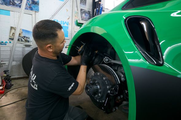 Mechanic working inside the front wheel well of a bright green sports car in a workshop