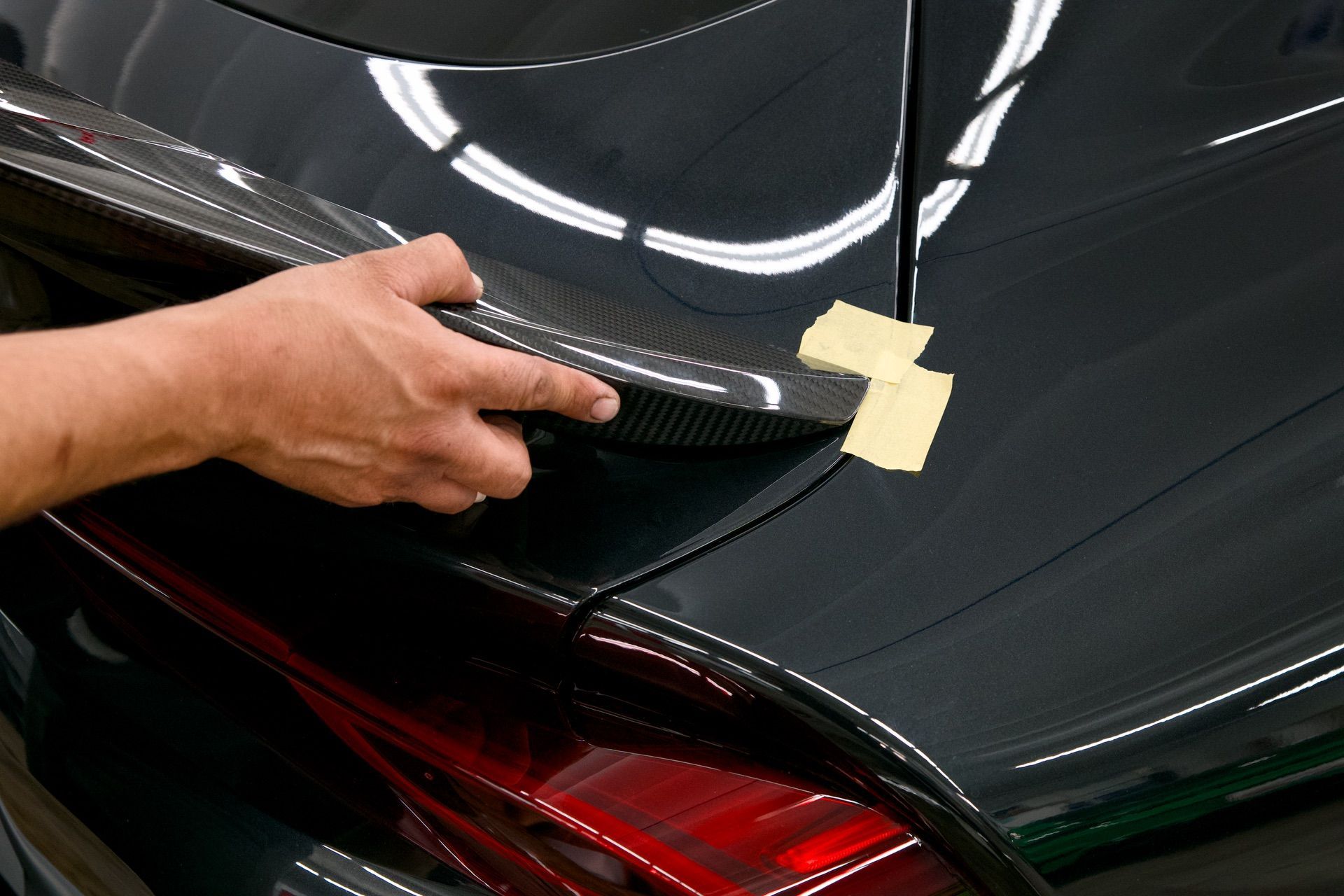 Hand polishing a black car trunk with tape marking a repair area