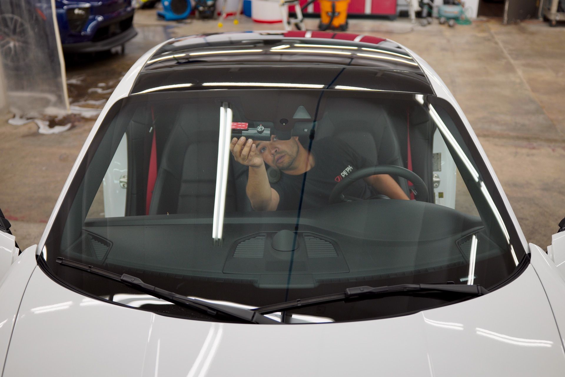 Person seen through a car windshield holding a phone inside a white car in a garage