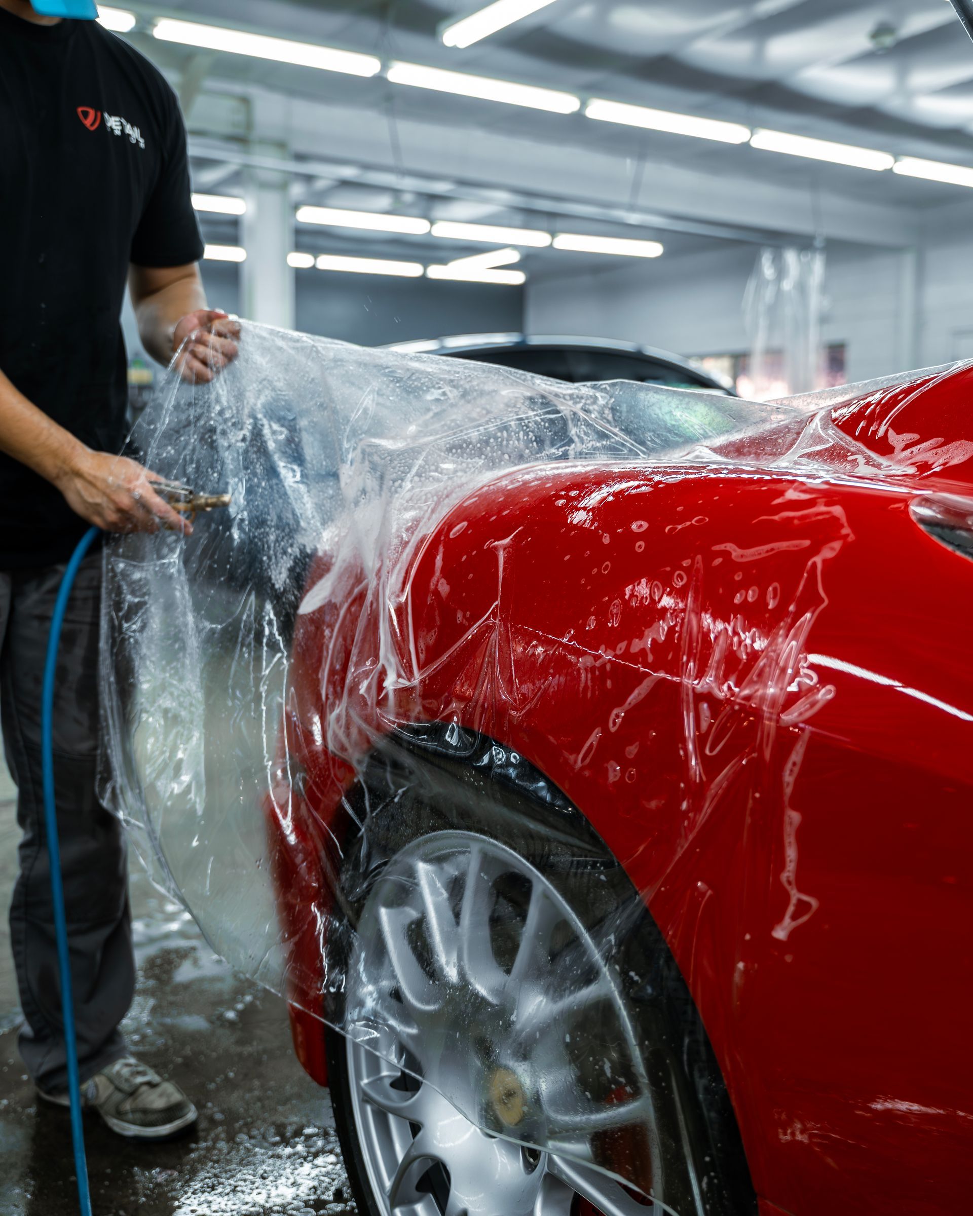 Person washing a red sports car with a hose in a garage.