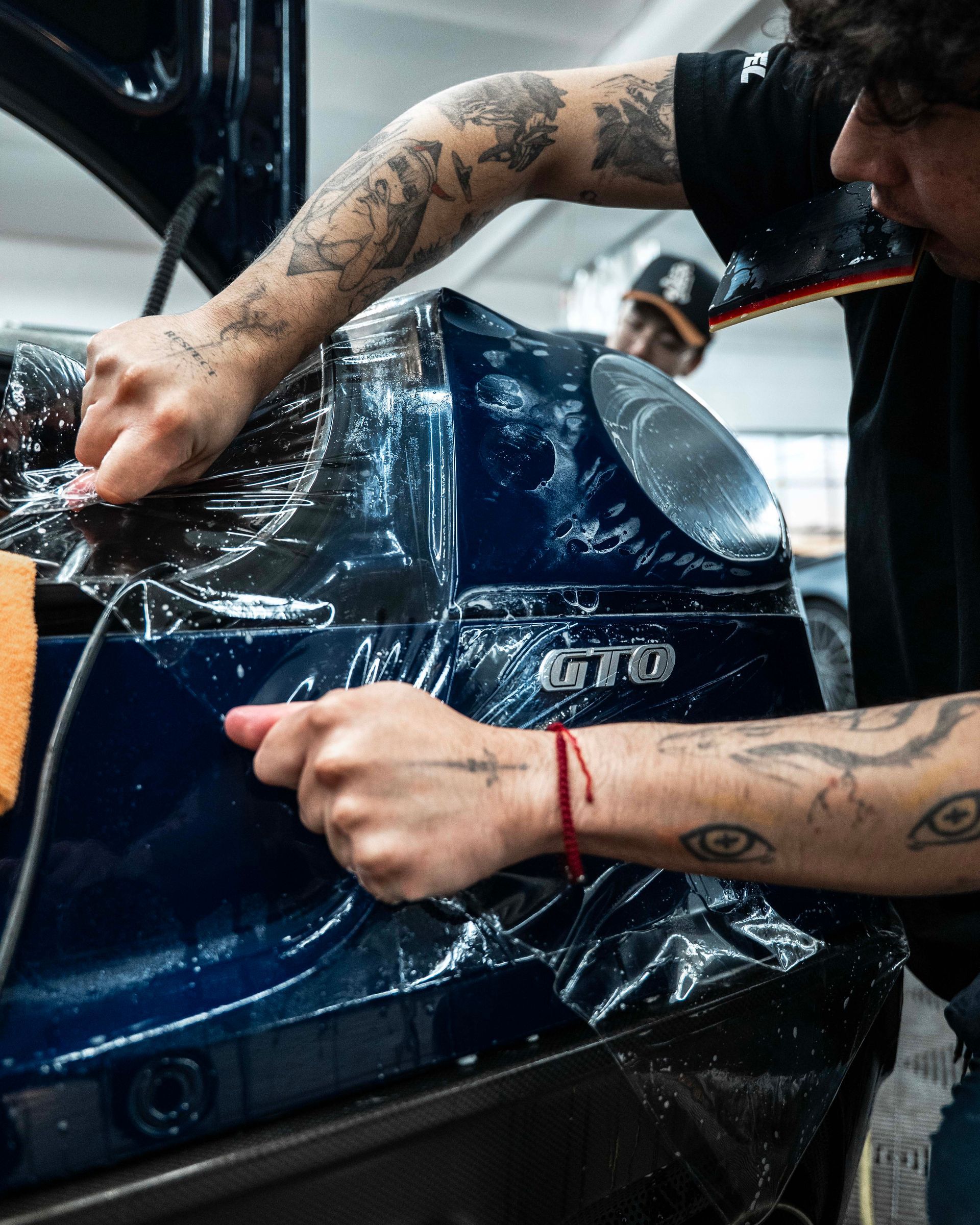 Person applying clear protective film to a blue car bumper in a workshop