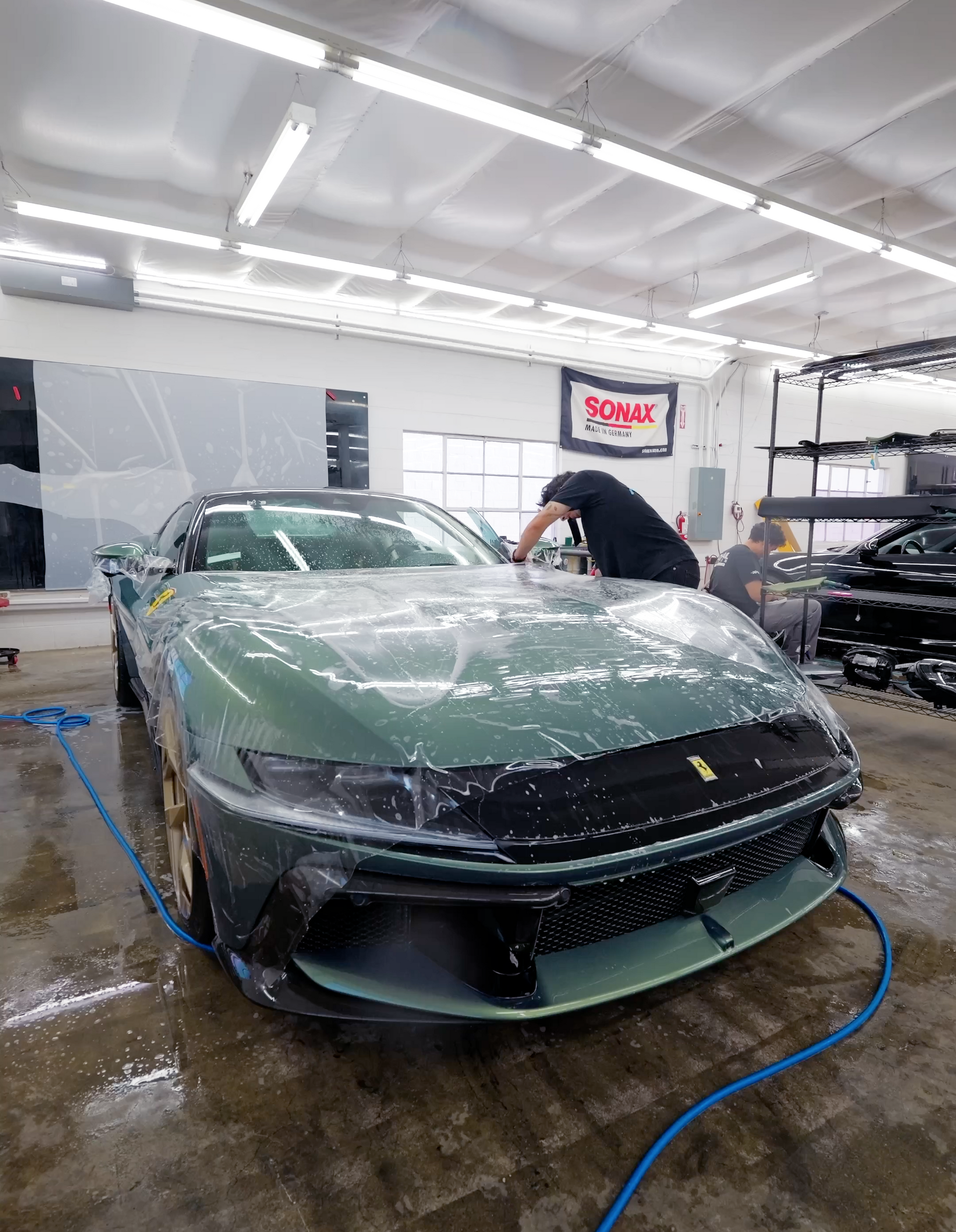 Green sports car being washed in a car detailing shop, with a person scrubbing the hood.