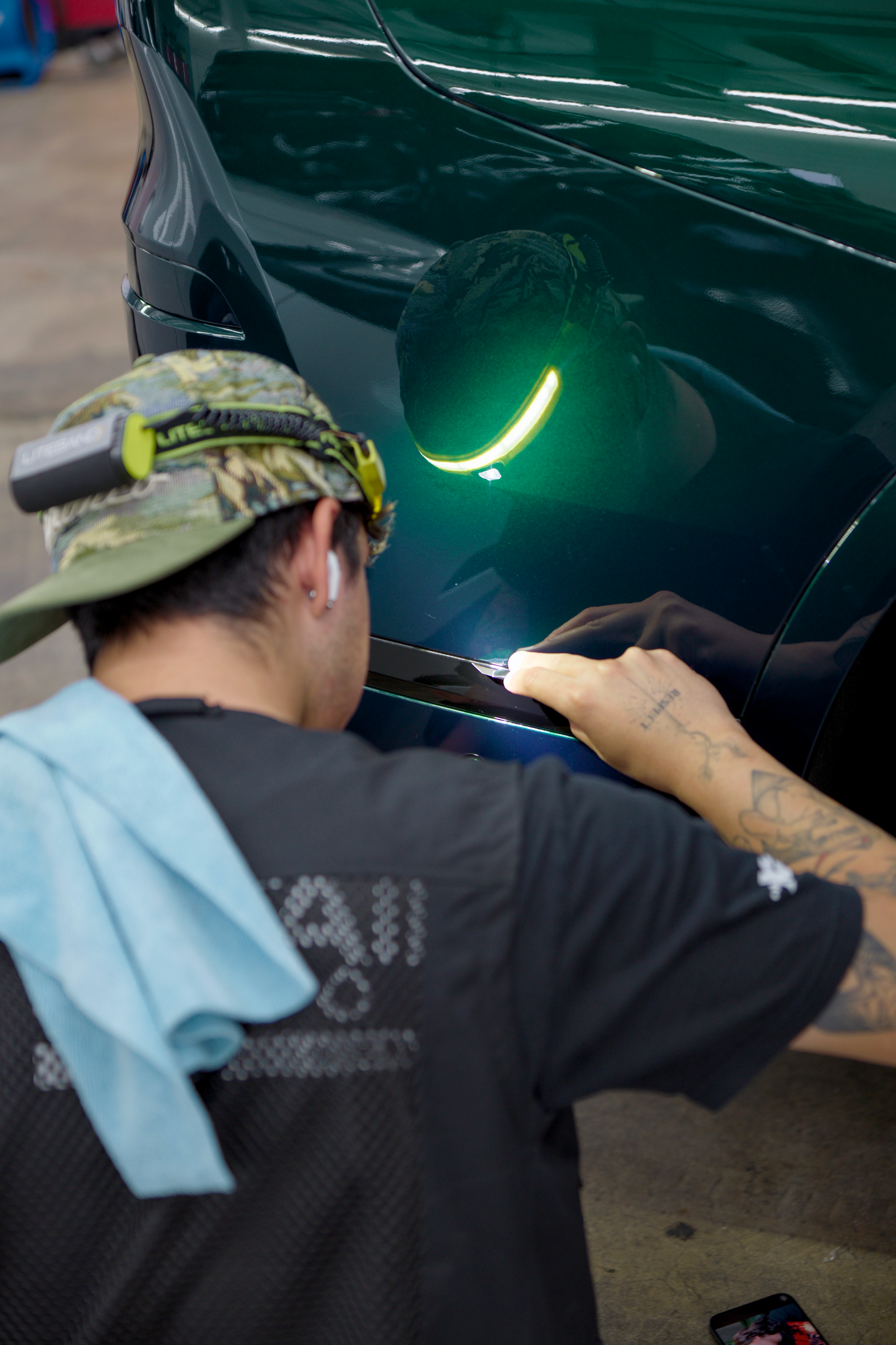 Mechanic polishing a dark green car’s front bumper in a garage