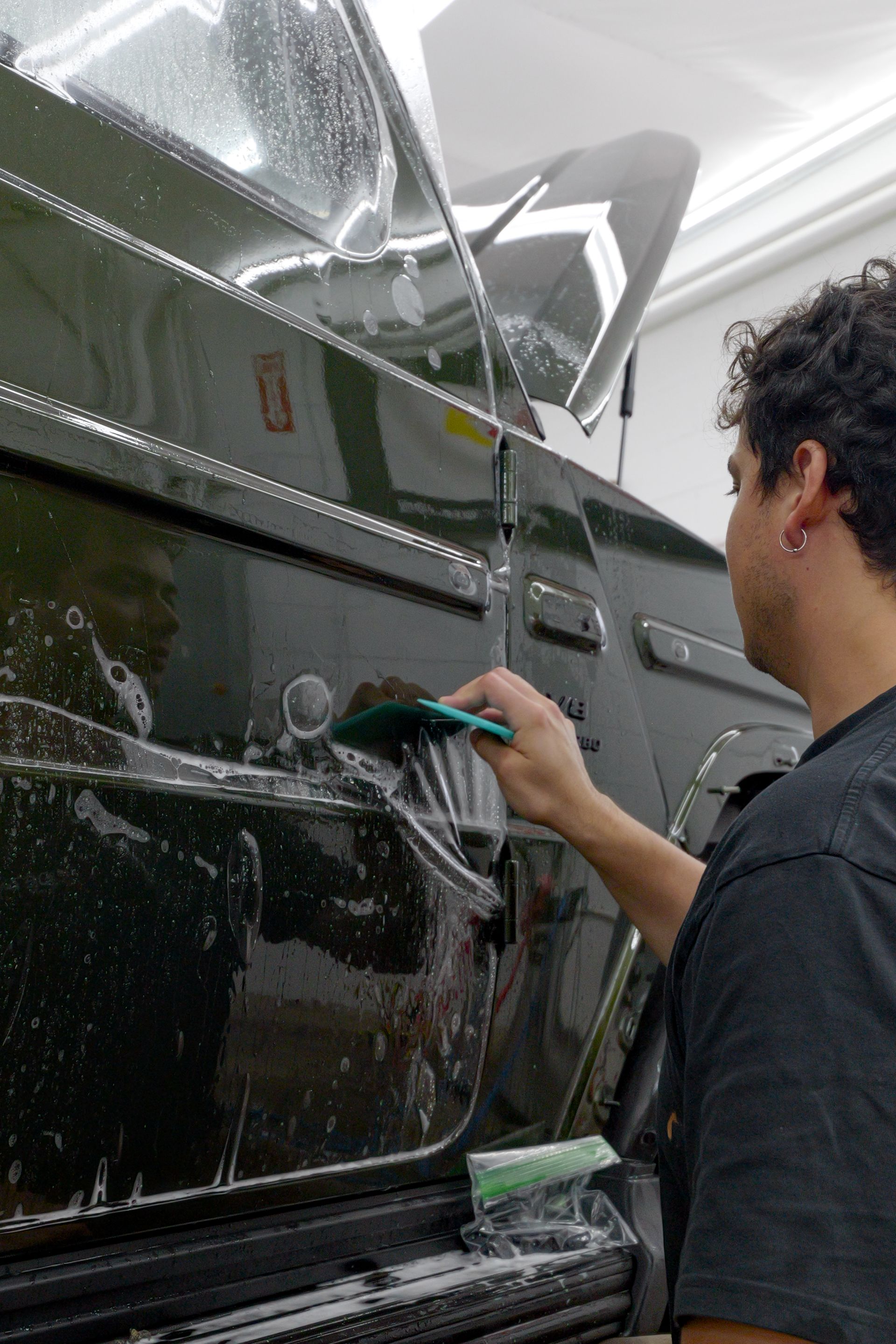 Person washes a dark van with a sponge in a car wash bay