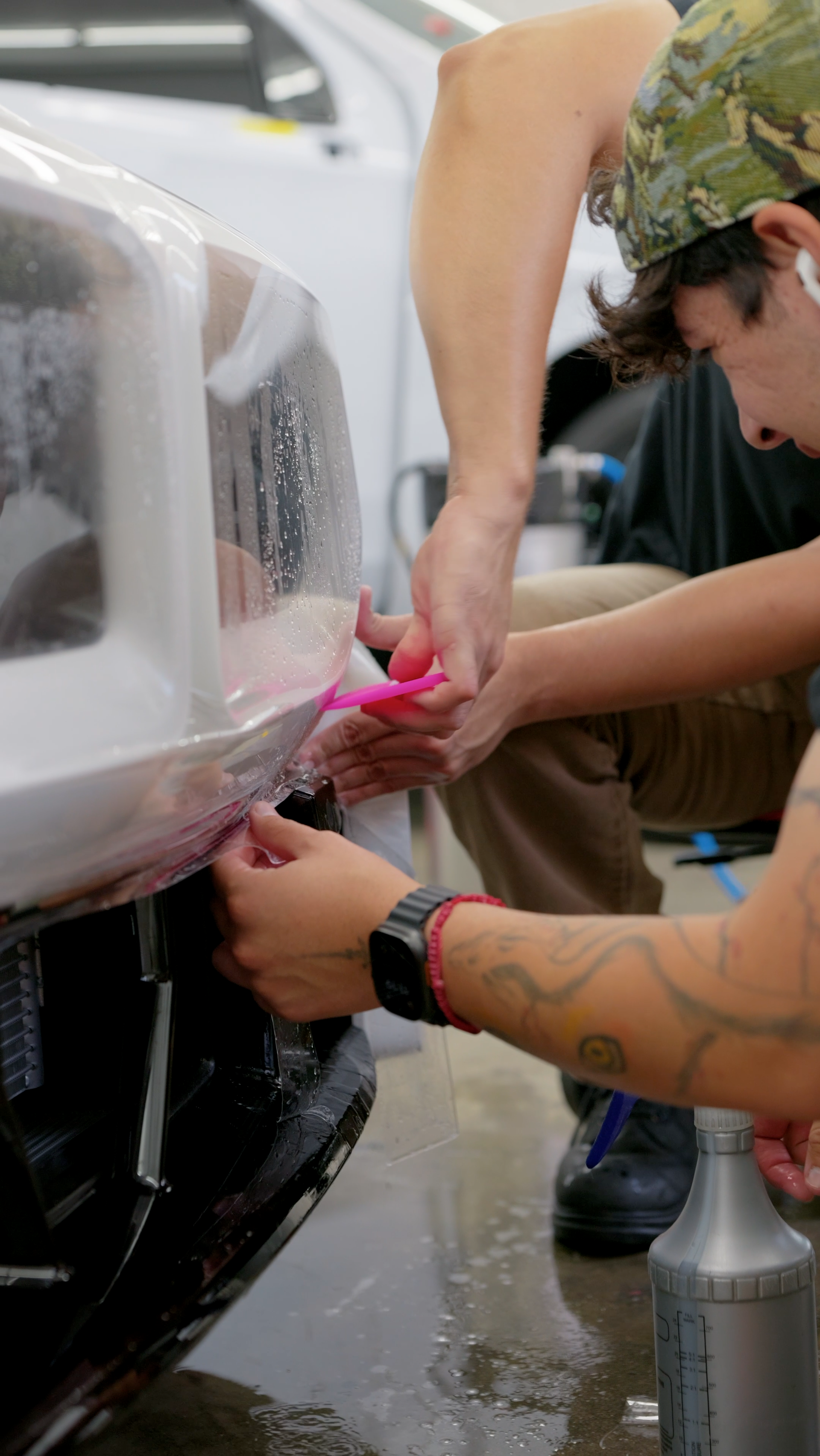 Person wrapping pink tape around a car bumper in a garage