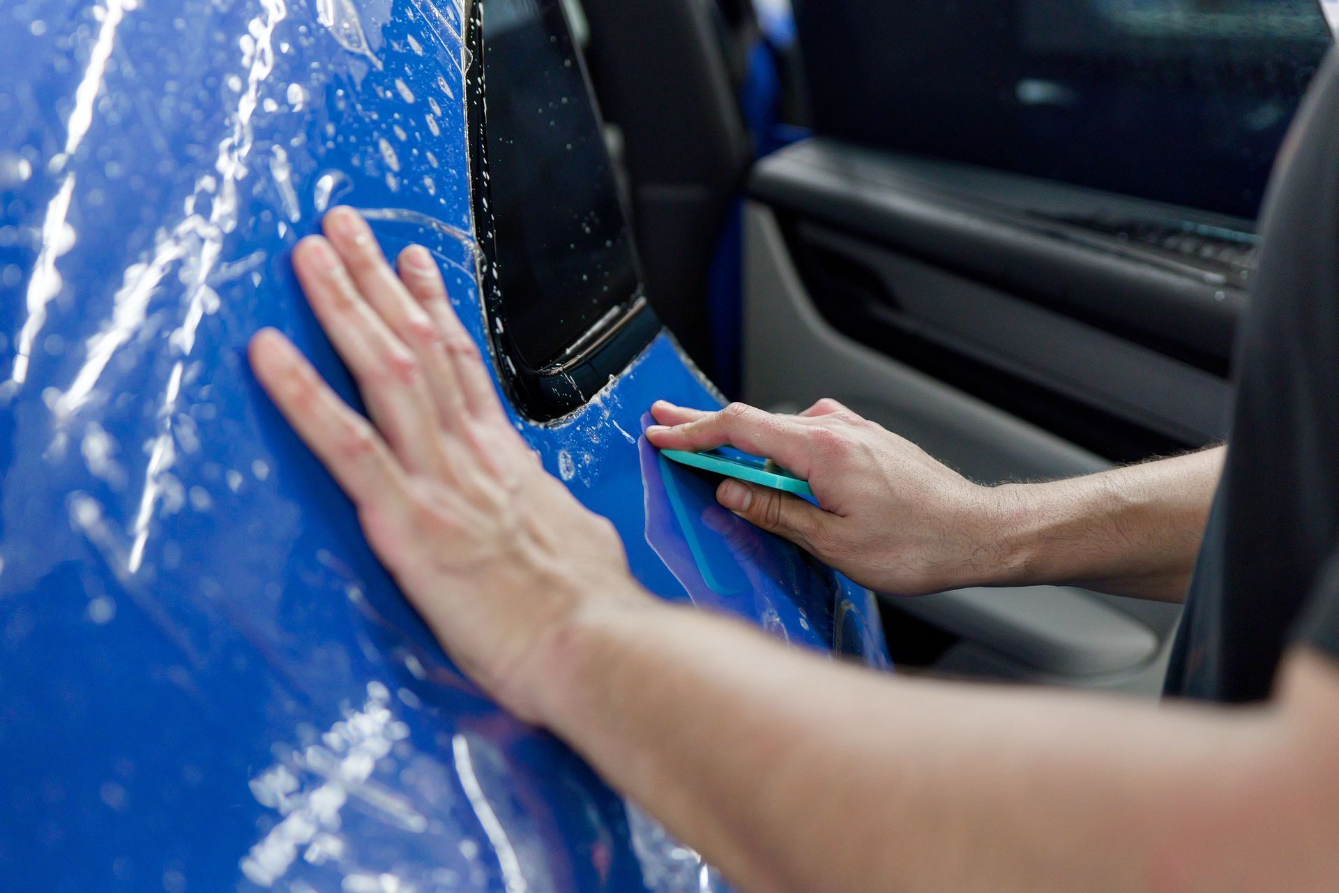 Hands using a squeegee to apply blue vinyl wrap to a car door